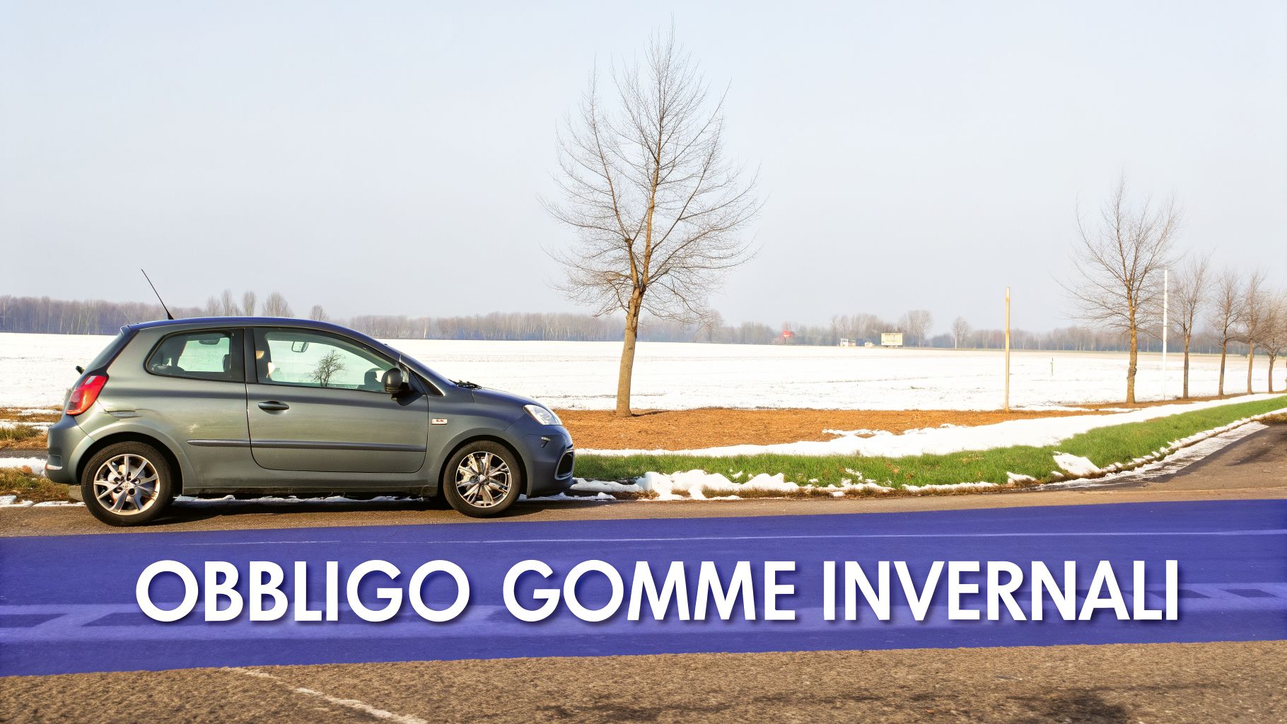 Un'auto grigia su una strada di campagna con campi innevati e alberi spogli, evidenziando l'obbligo di gomme invernali.