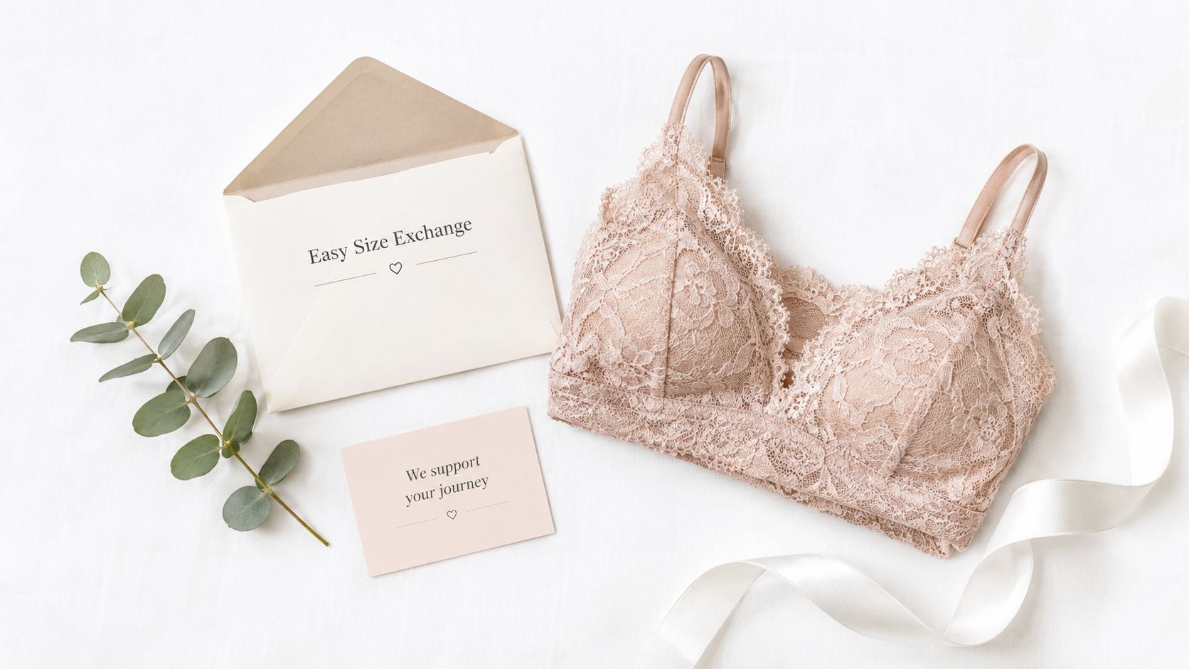 A lace bralette, an open envelope with text, a small note, and eucalyptus branches on white fabric.