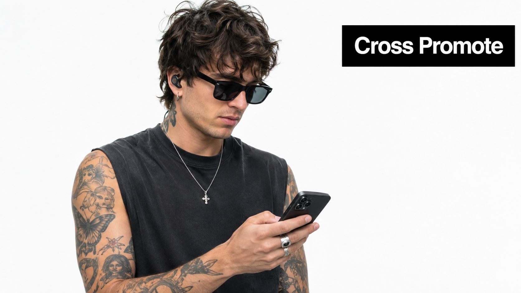A stylish young man with tattoos looking at his smartphone while wearing sunglasses and wireless earbuds.