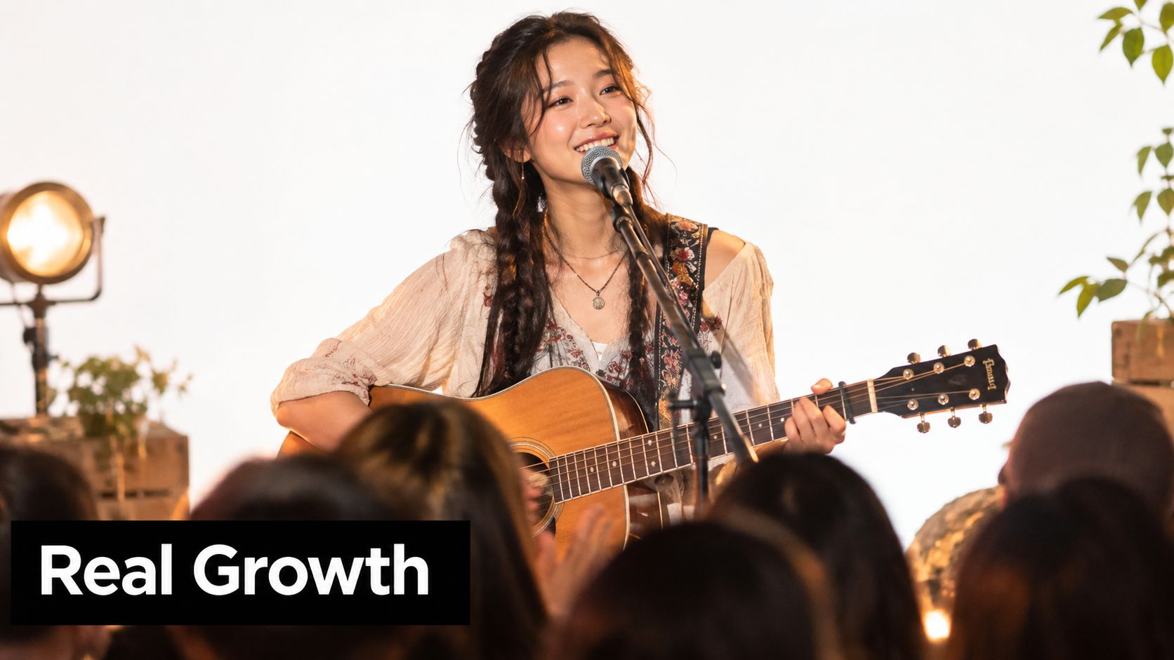 A smiling young female musician playing an acoustic guitar and singing into a microphone on stage.