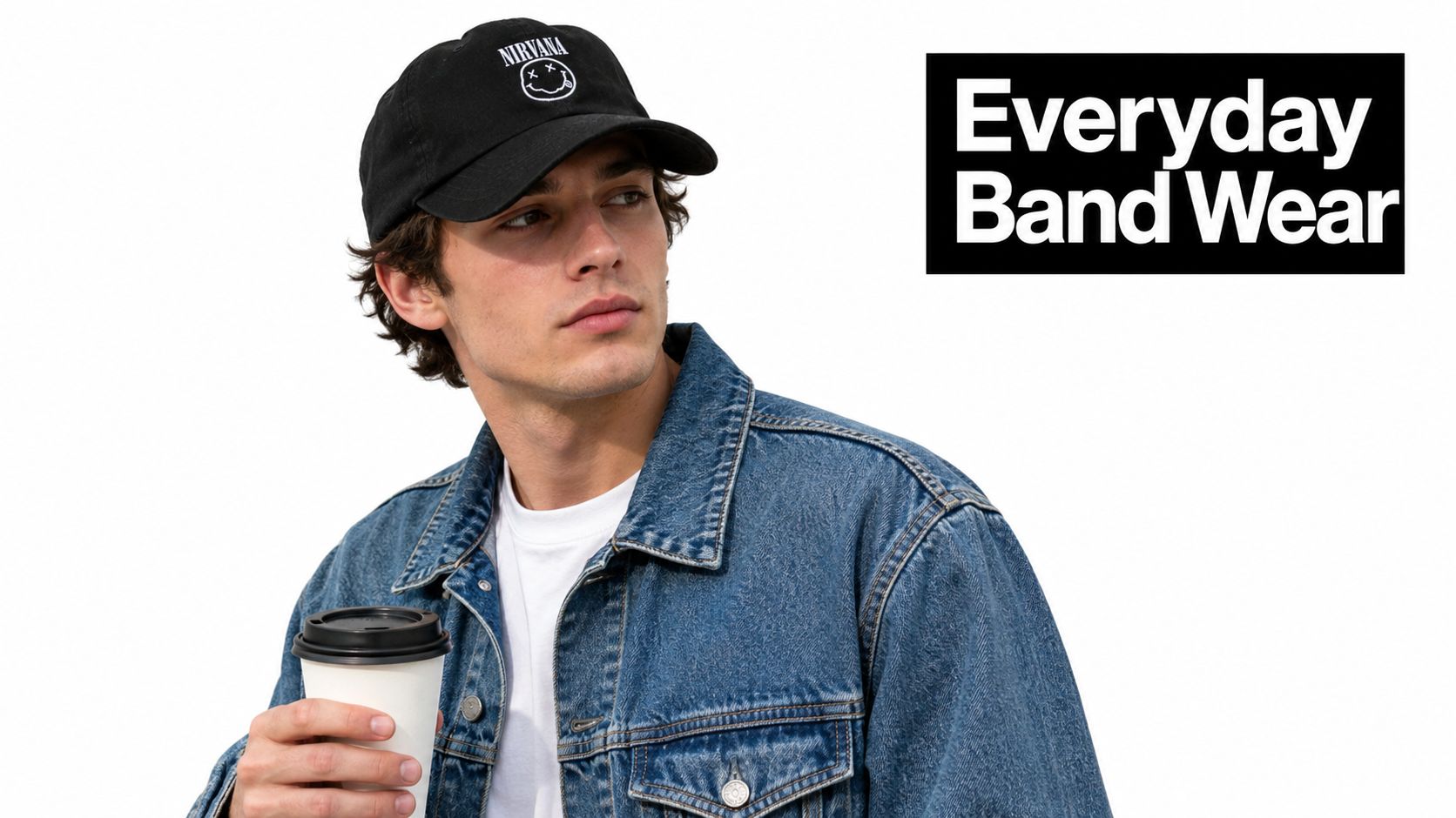 A young man wearing a black Nirvana baseball cap and denim jacket holding a coffee cup.