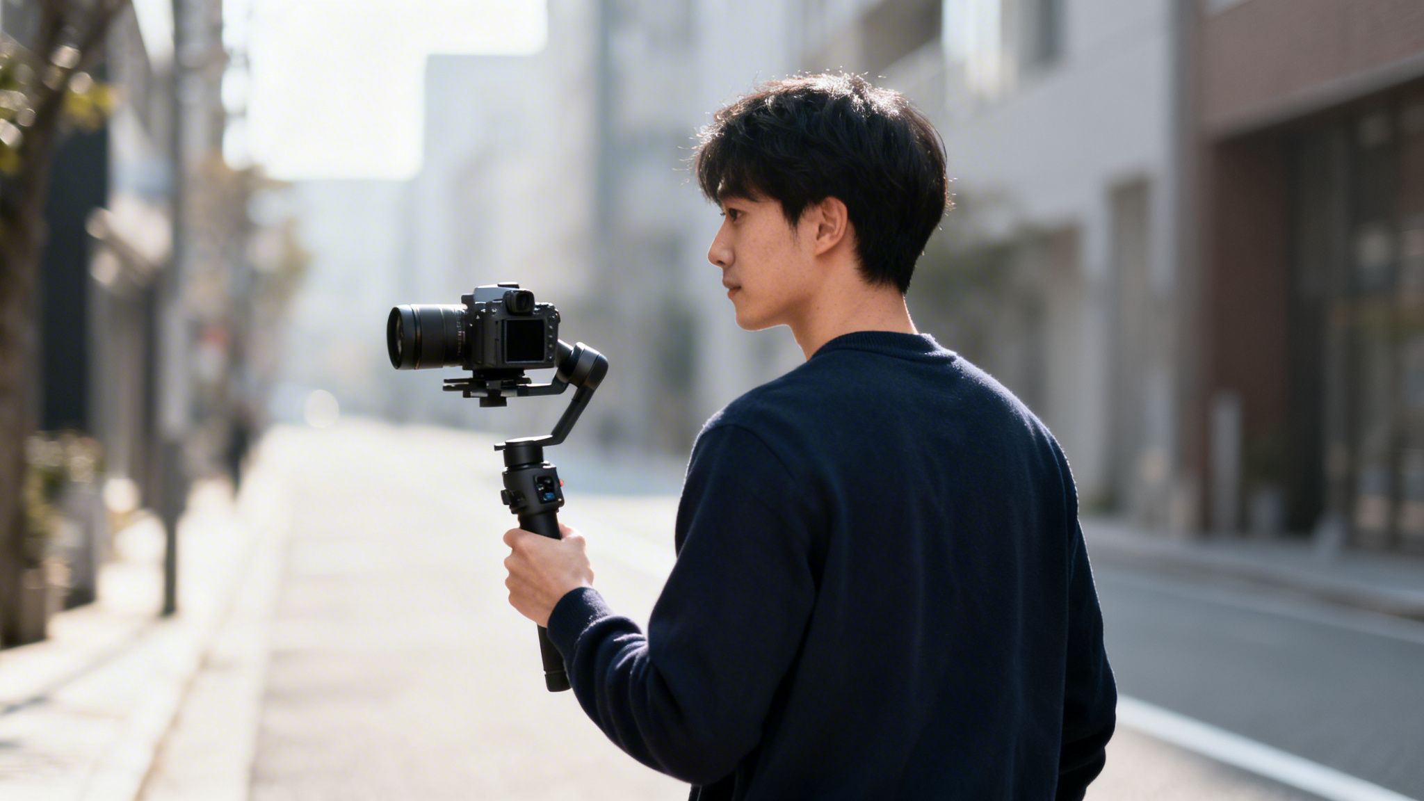 A young man outdoors holding a mirrorless camera mounted on a gimbal, preparing to film.