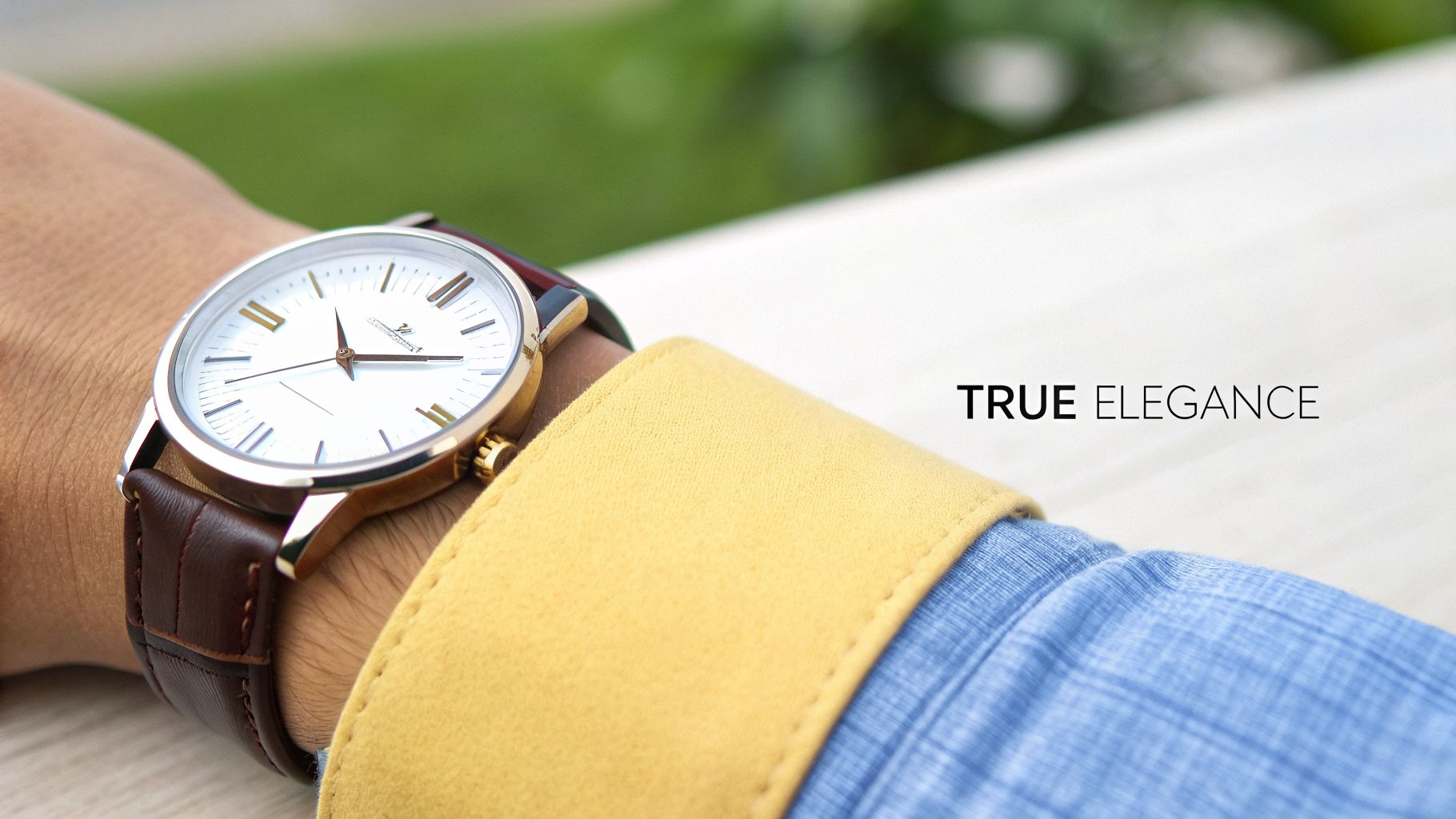 Close-up of a classic gold-toned watch with a white dial and brown leather strap on a person's wrist, with "TRUE ELEGANCE".