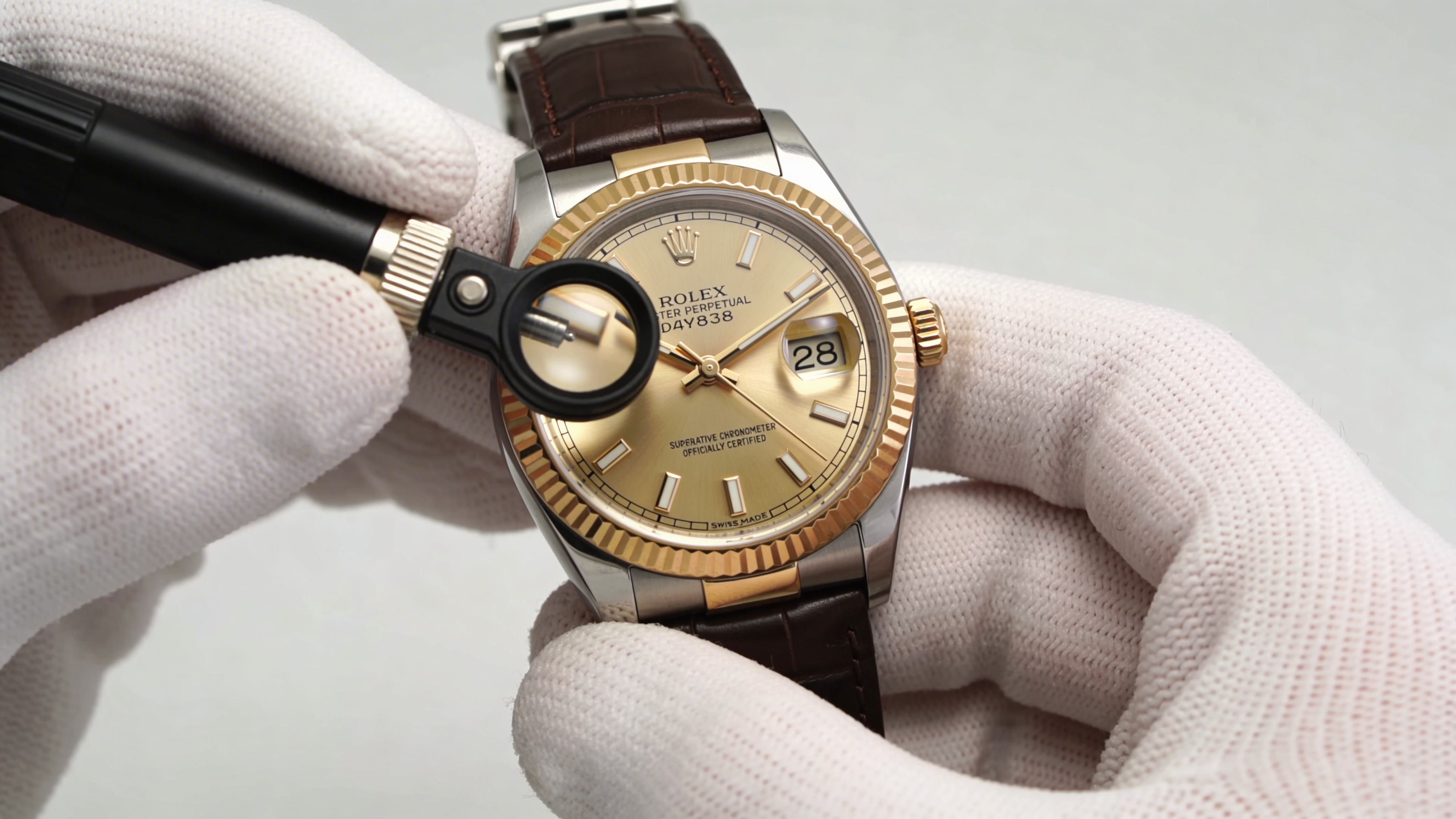 A gloved hand inspecting a luxury Rolex watch with a jeweler's loupe for authentication and quality control.