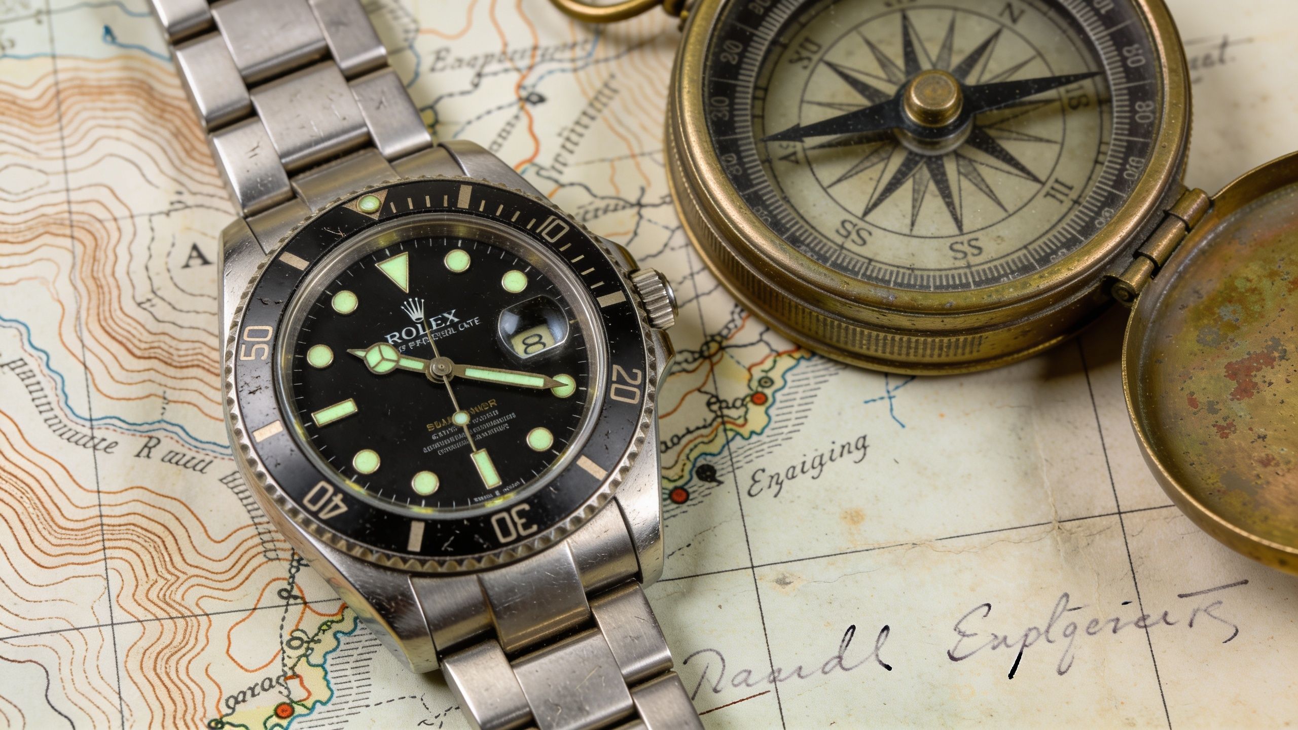A Rolex Submariner wristwatch resting on a vintage topographic map alongside an antique brass magnetic compass.