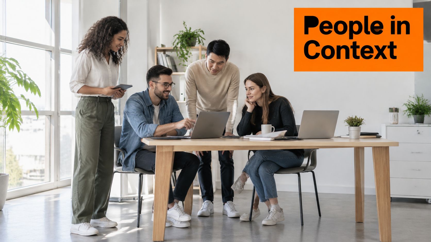 A diverse team of four young professionals collaborating around a wooden table with laptops in a bright office.