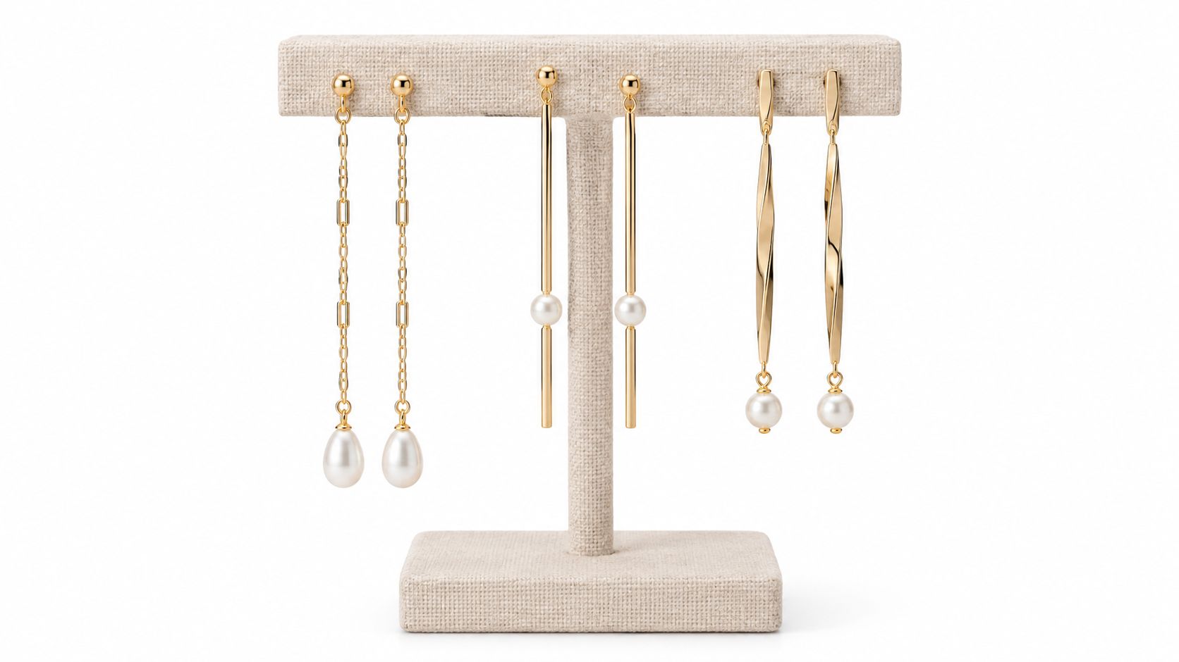 A beige jewelry display stand holding three pairs of elegant long gold earrings with white pearls.