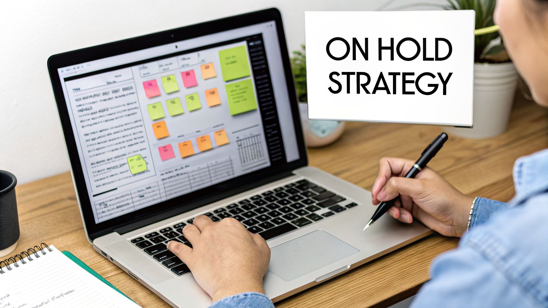 Professional planning an 'ON HOLD STRATEGY' on a laptop with digital sticky notes and a pen.