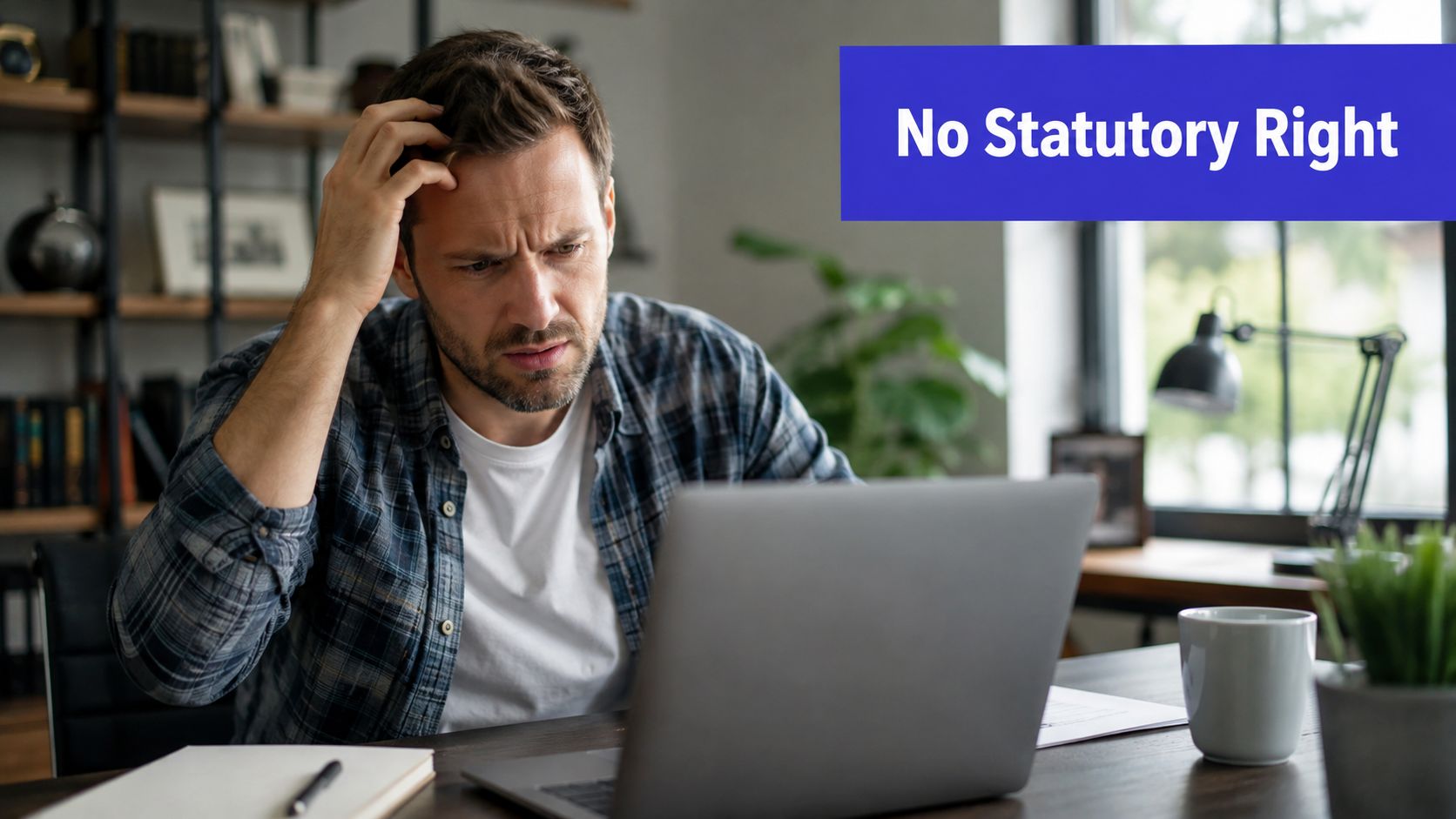 A concerned man looking at his laptop screen while sitting at a wooden office desk.