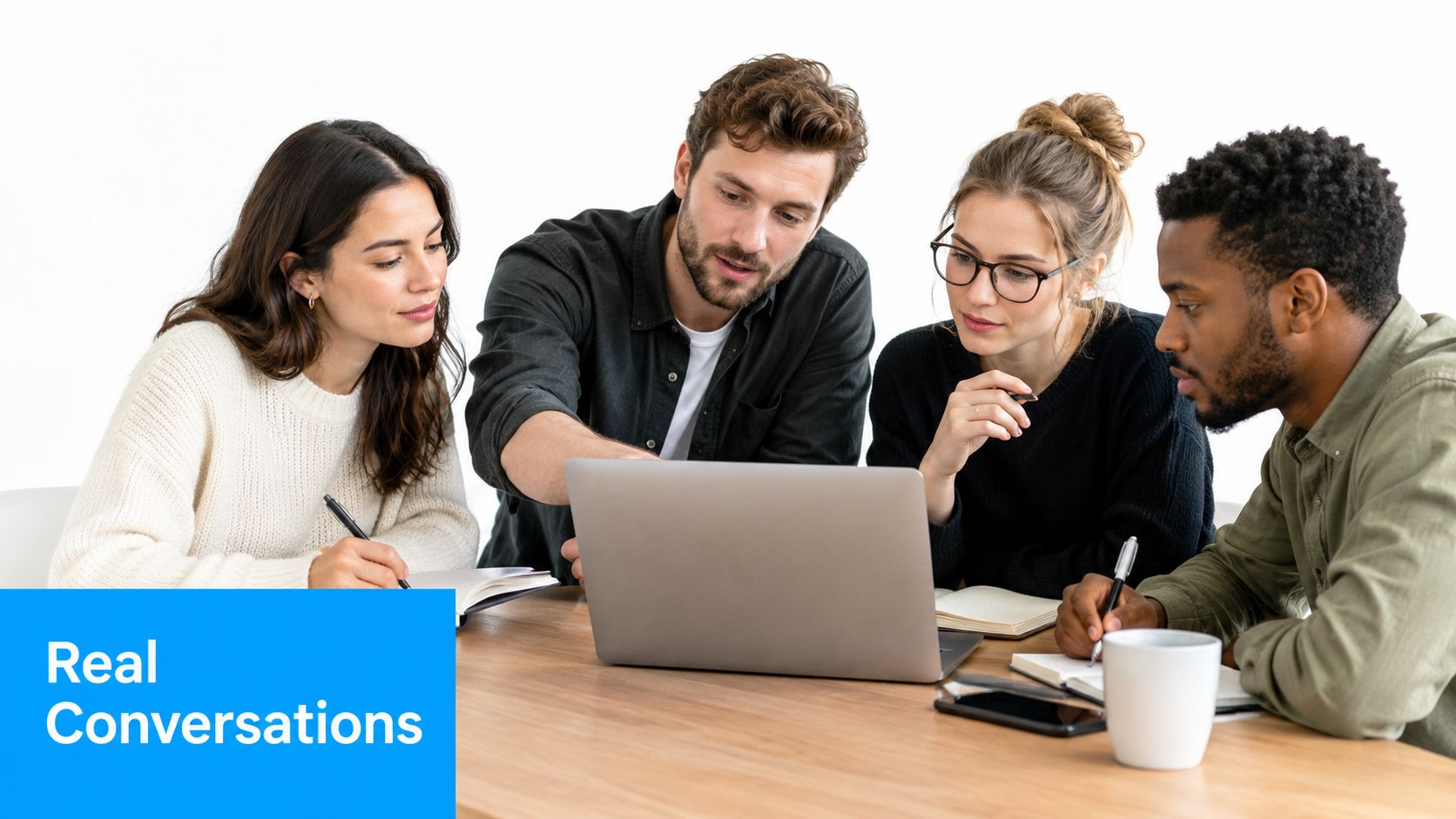 A diverse group of four young professionals collaborating and having a real conversation around a laptop.