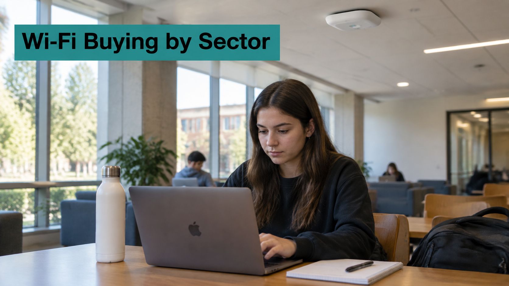 A student working on a laptop at a table in a modern university library study space.
