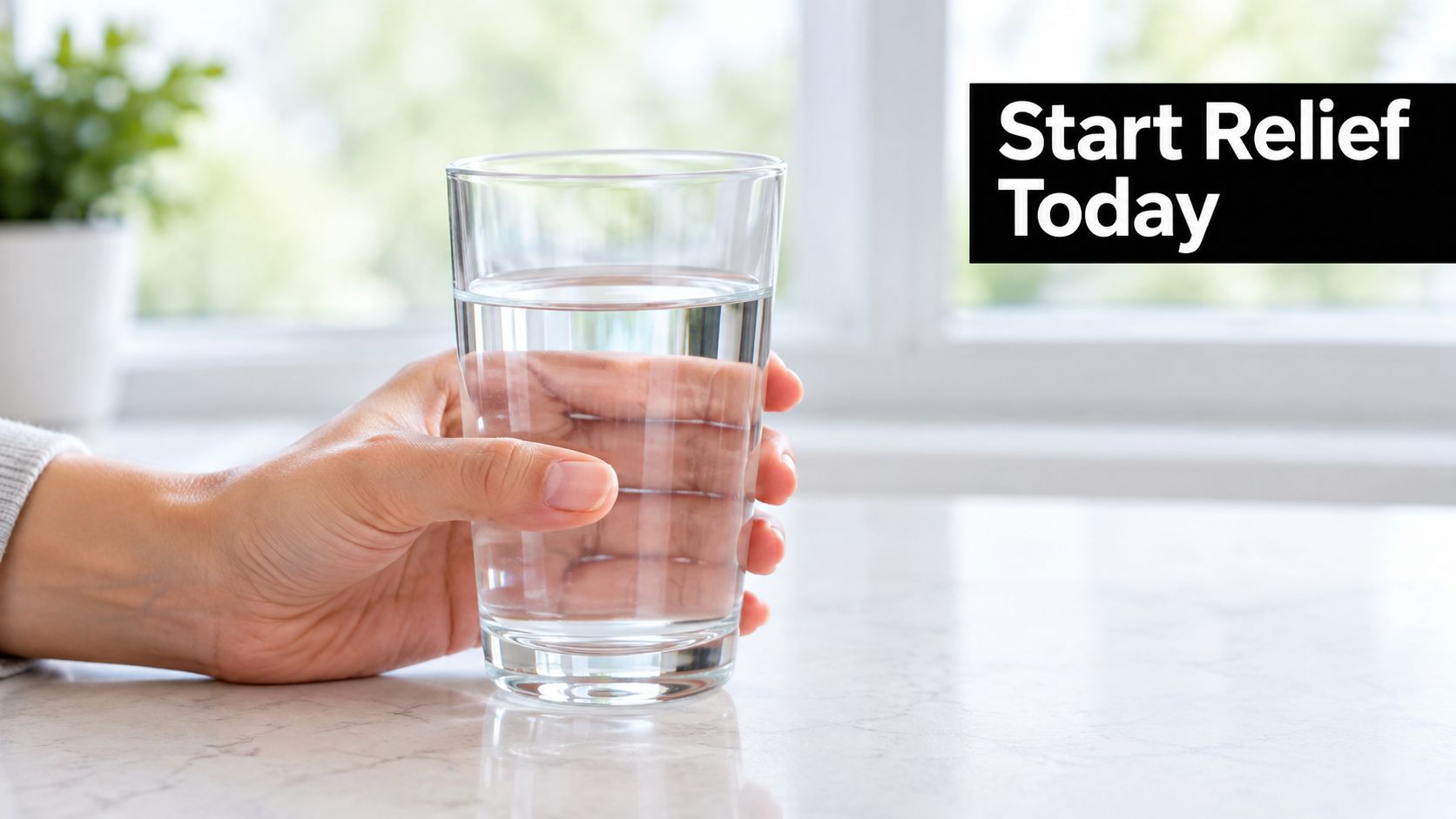 A hand holding a clear glass of water on a marble counter to suggest relief from tooth sensitivity.