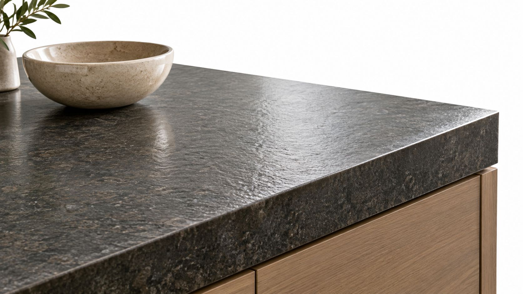 A close-up view of a textured dark stone countertop sitting on a light wood kitchen cabinet.