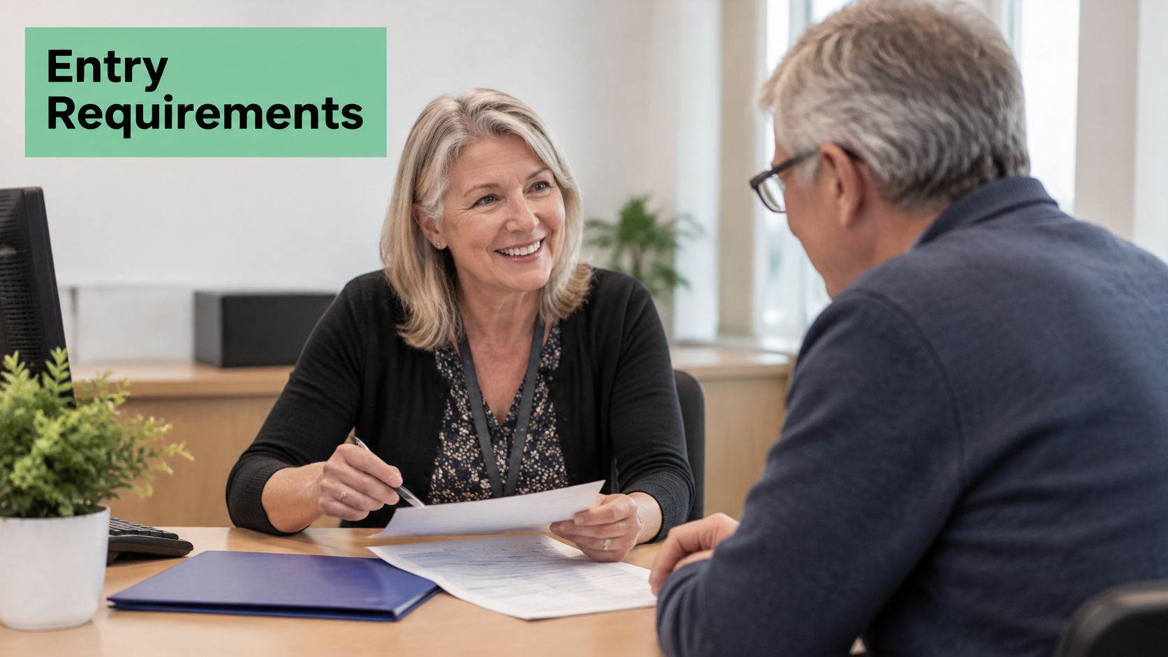 A smiling professional advisor sits at a desk discussing paperwork with a student during an office consultation.