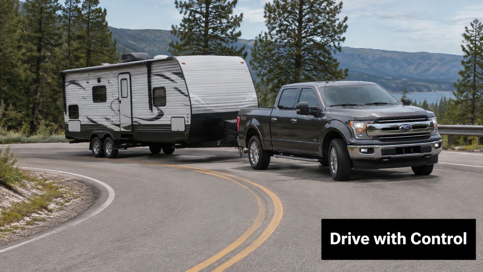 A modern grey Ford pickup truck towing a large white camping trailer along a winding mountain road.