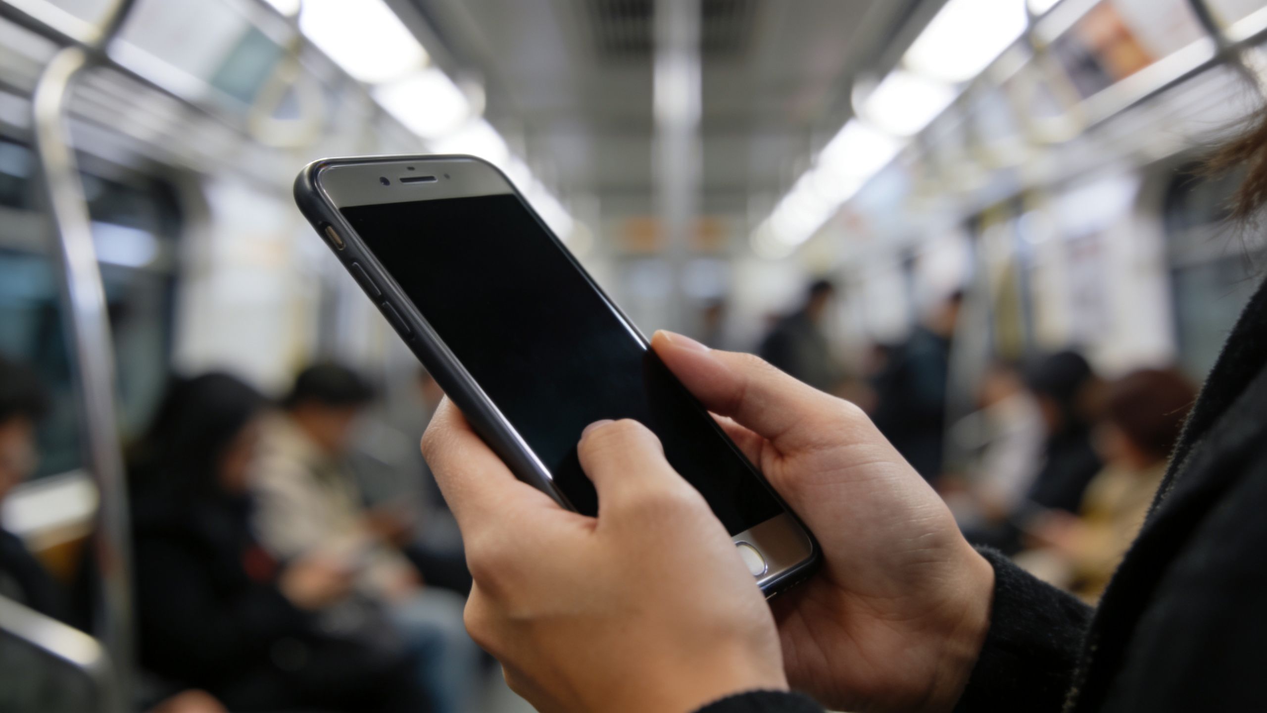 Ένα άτομο κρατά ένα smartphone μέσα σε συρμό μετρό, προστατεύοντας την οθόνη του με ειδικό φίλτρο ιδιωτικότητας.