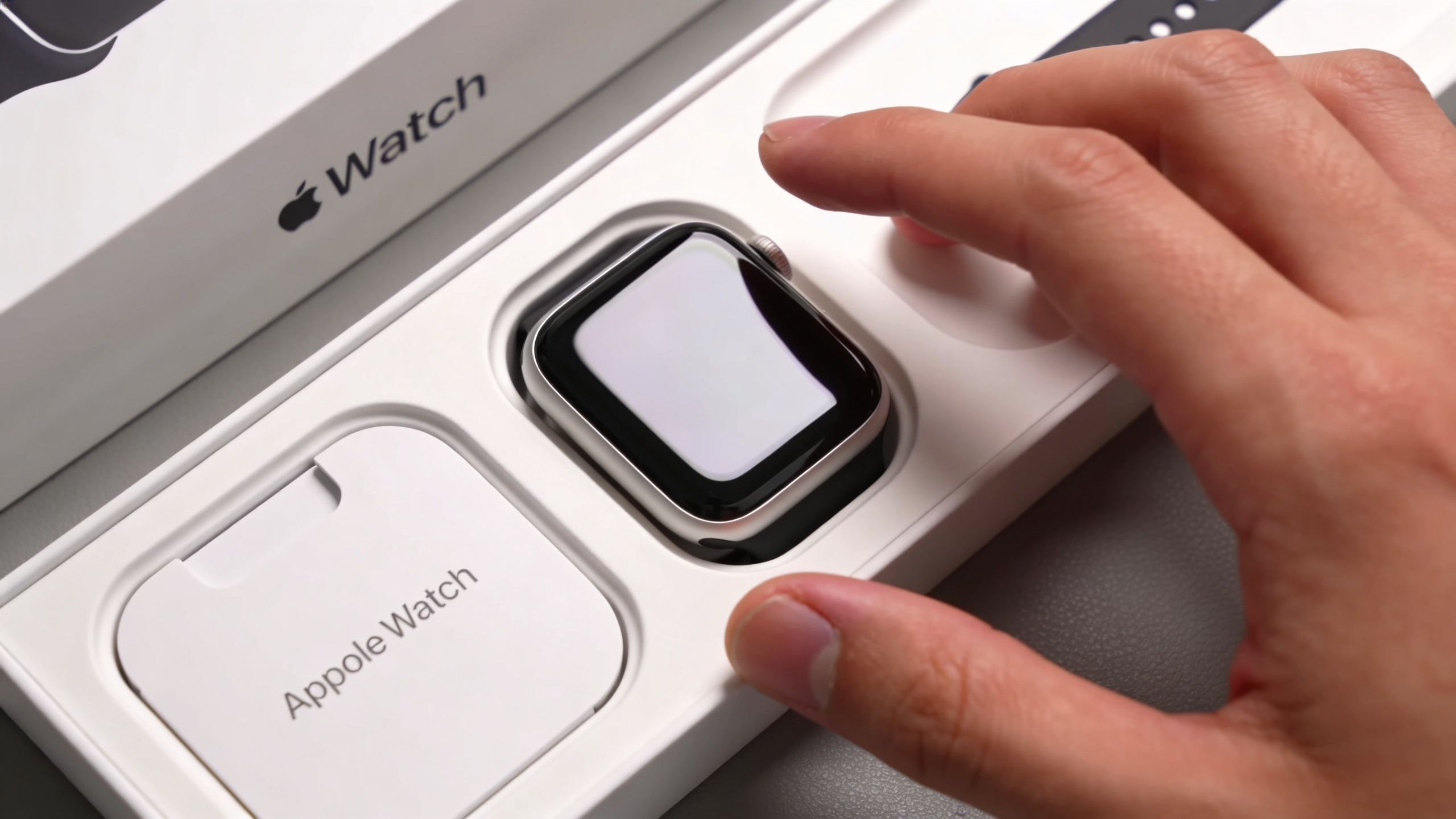 Ένα χέρι αγγίζει ένα καινούργιο Apple Watch που βρίσκεται μέσα στη λευκή συσκευασία του για ξεπακετάρισμα.