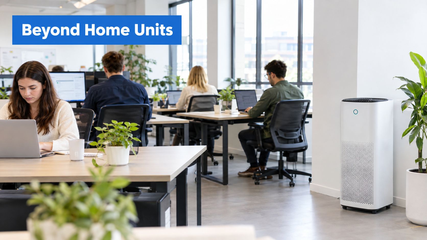 A sleek white air purifier standing in a modern, sunlit office environment with employees working at desks.