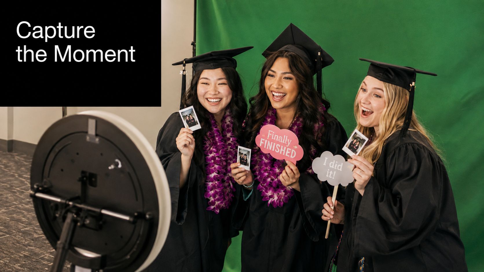 Three happy female graduates wearing academic caps and graduation gowns taking photos at a photo booth.