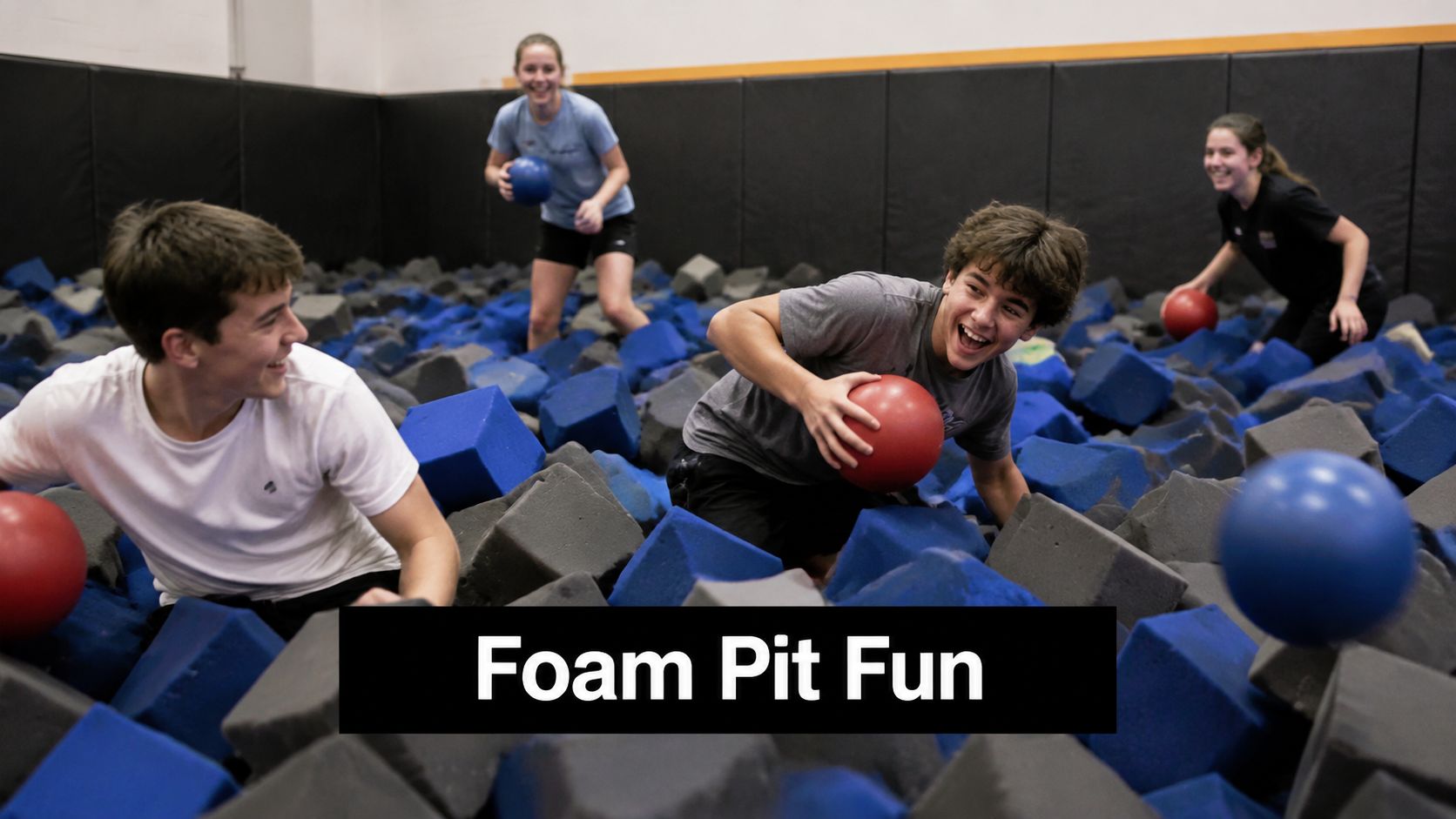 A group of happy teenagers playing with balls inside a large foam pit at an activity center.