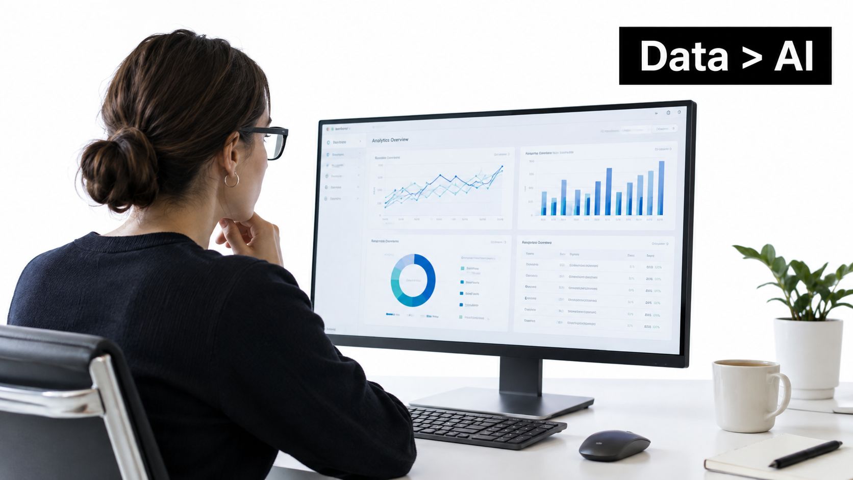 A woman in a black sweater sitting at a desk looking at data charts on a computer monitor.