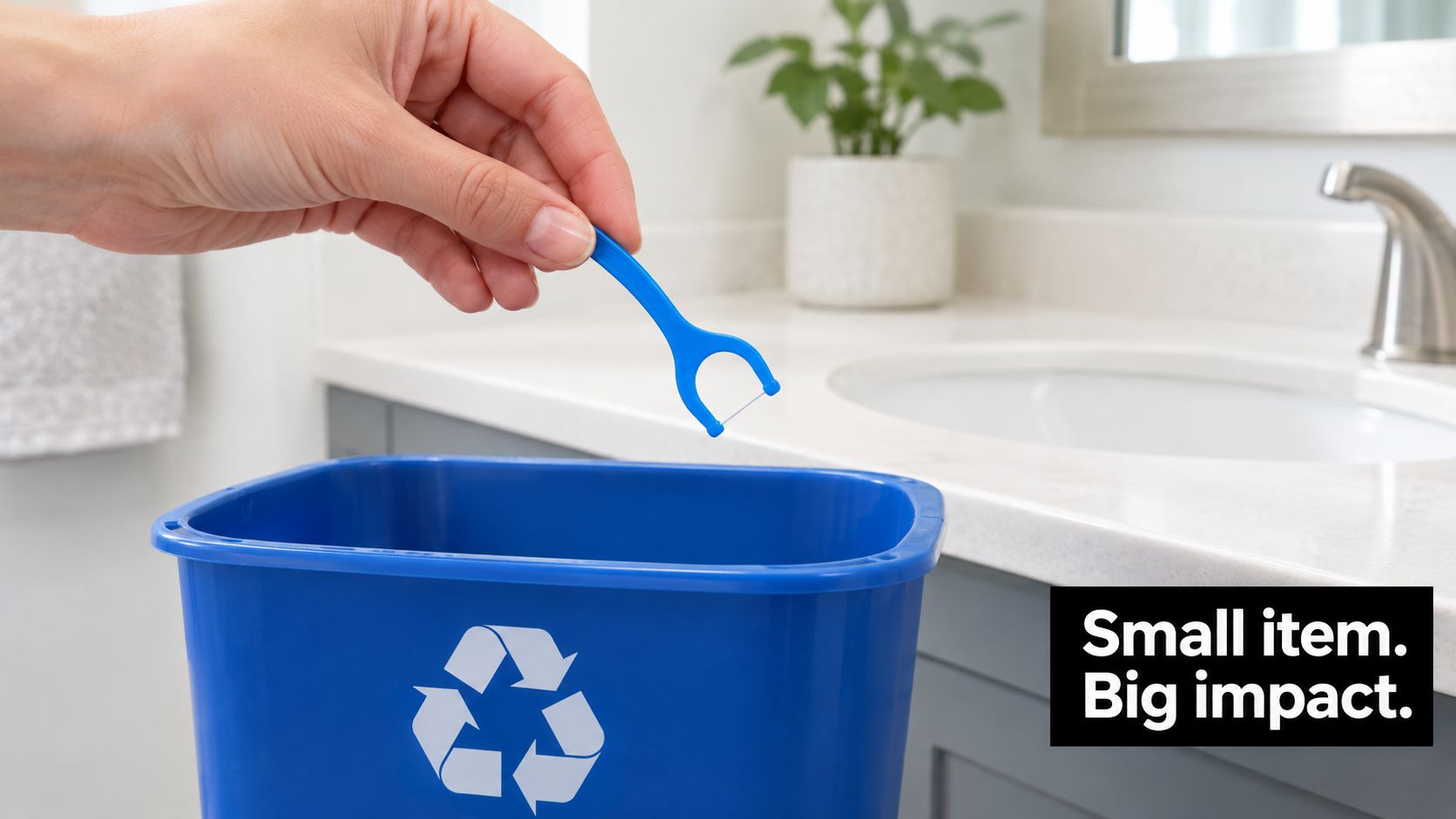 A hand holding a plastic dental floss pick over a blue recycling bin in a bathroom.