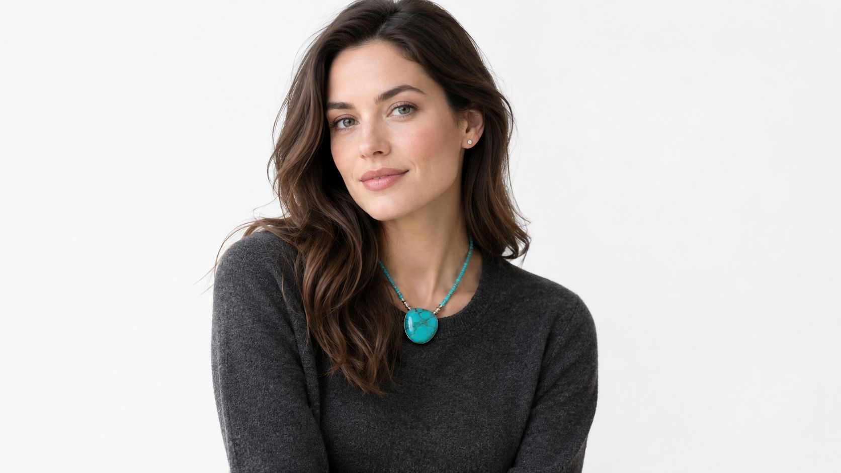 A beautiful woman wearing a turquoise pendant necklace against a simple white studio background