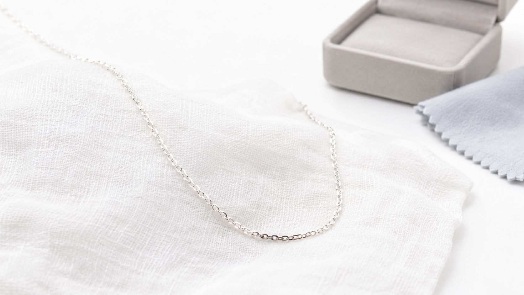 A delicate sterling silver chain necklace rests on a soft white cloth next to a jewelry box.