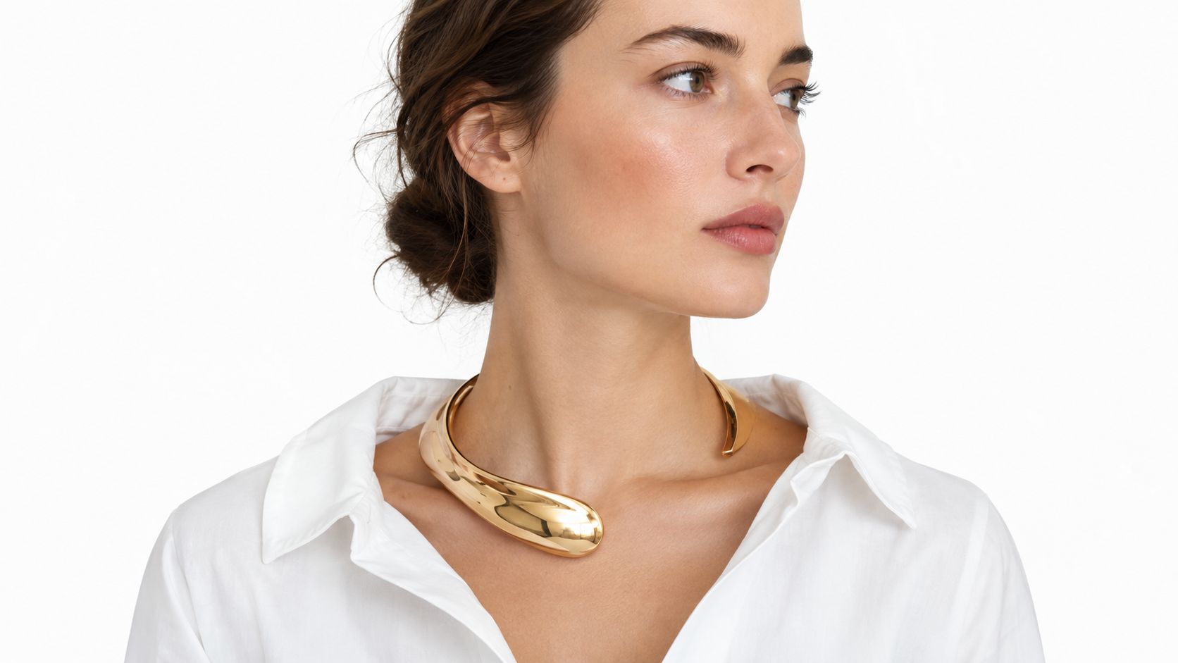 A woman wearing a modern, polished gold statement necklace over a crisp white button-down shirt.
