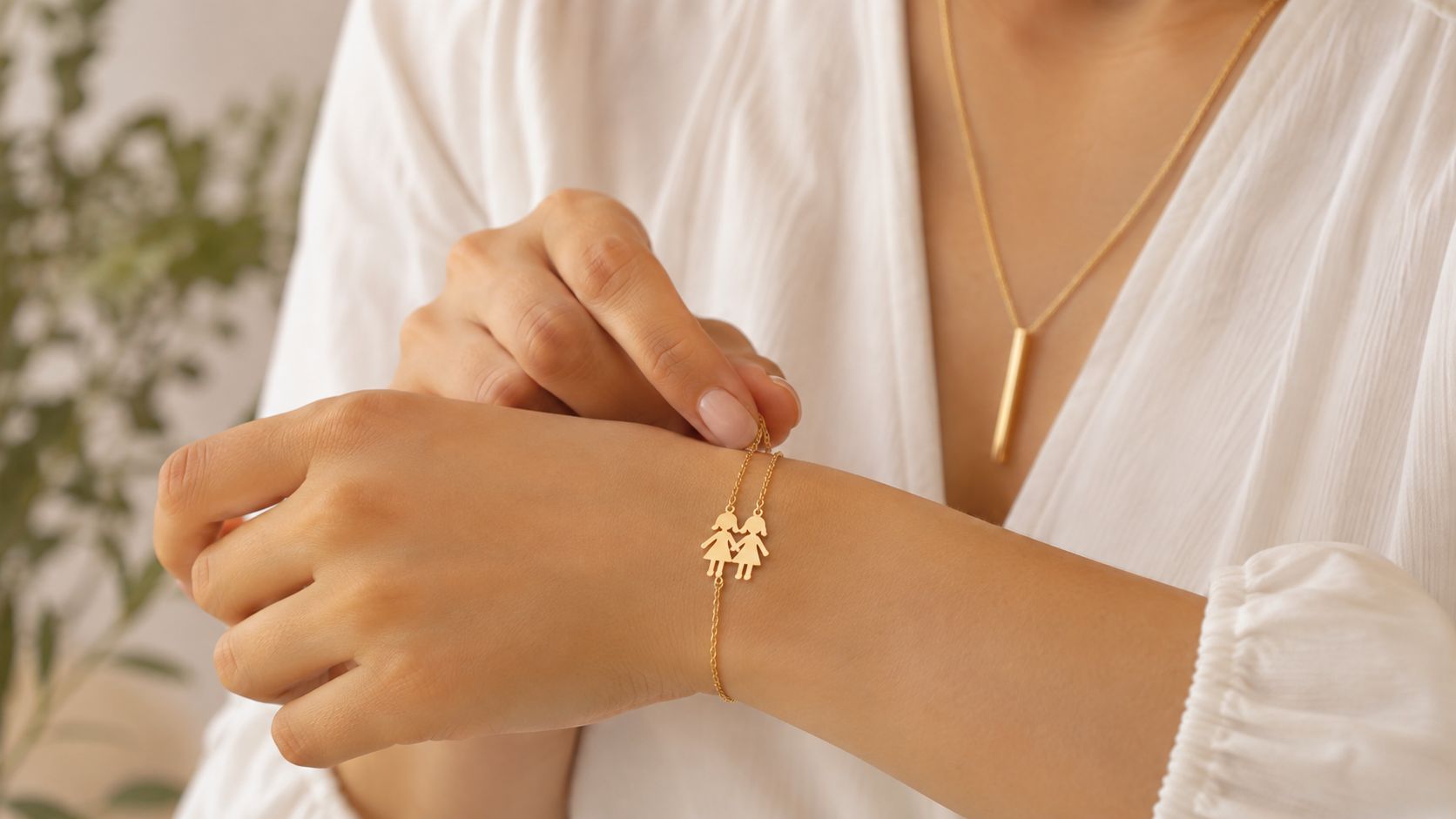 A woman wears a delicate gold bracelet featuring two small girl charms on her wrist.