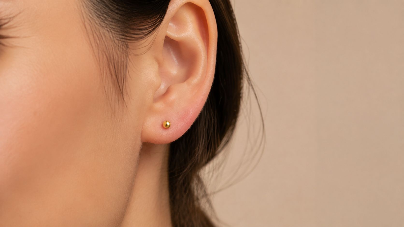 A close-up view of a woman wearing a simple, tiny gold stud earring in her earlobe.