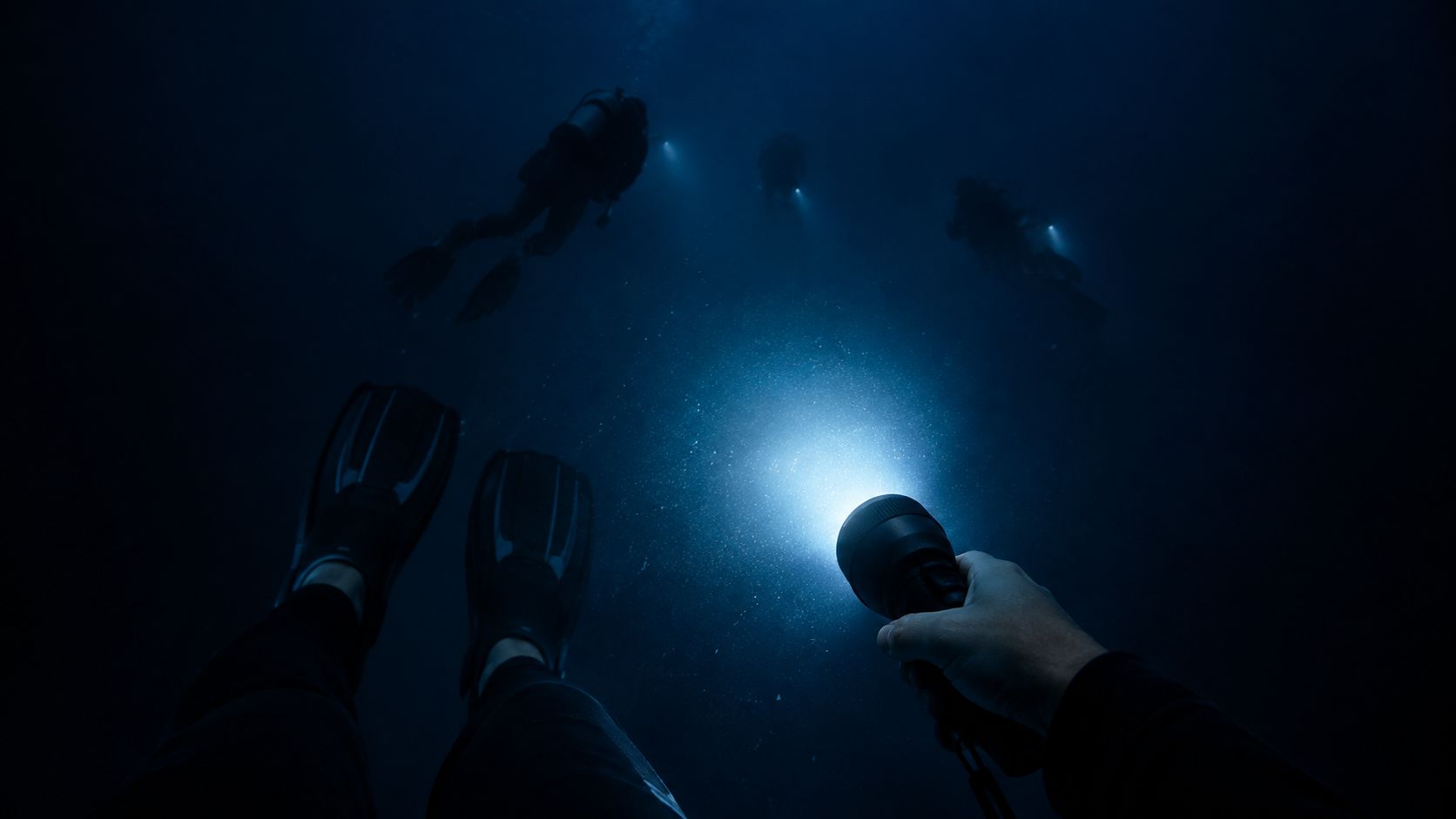 A first-person view of a diver holding a bright flashlight underwater with other divers swimming ahead.