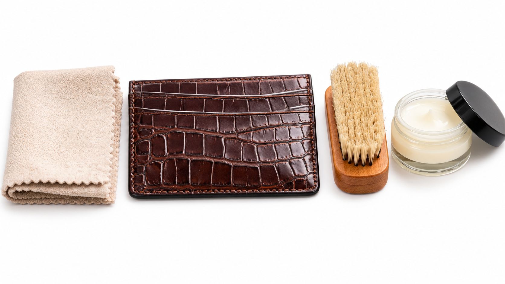 A leather crocodile card holder with a polishing brush, leather cream, and cleaning cloth for maintenance.