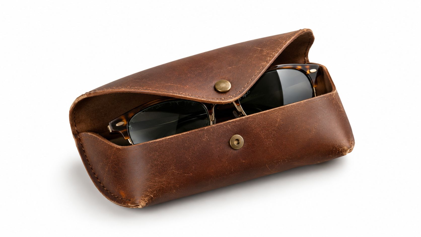 A rustic brown leather case with a brass button snap closure holding a pair of tortoiseshell sunglasses.