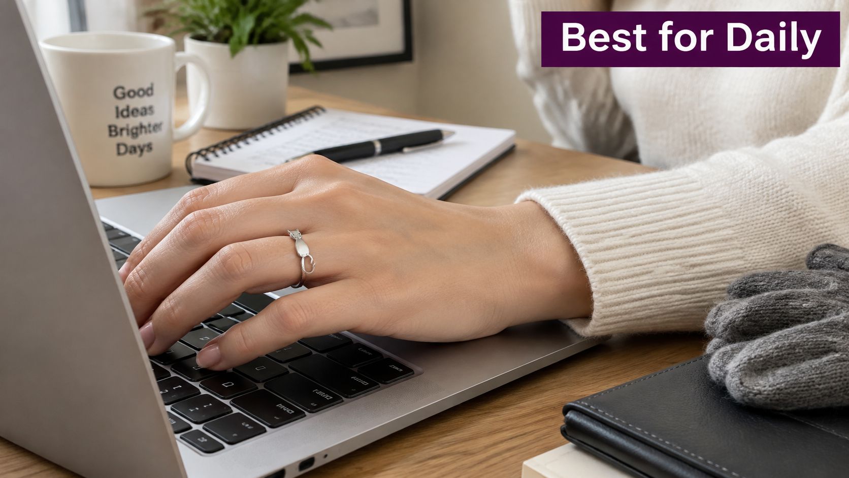 A person wearing a silver cat ring while typing on a laptop at a wooden desk.