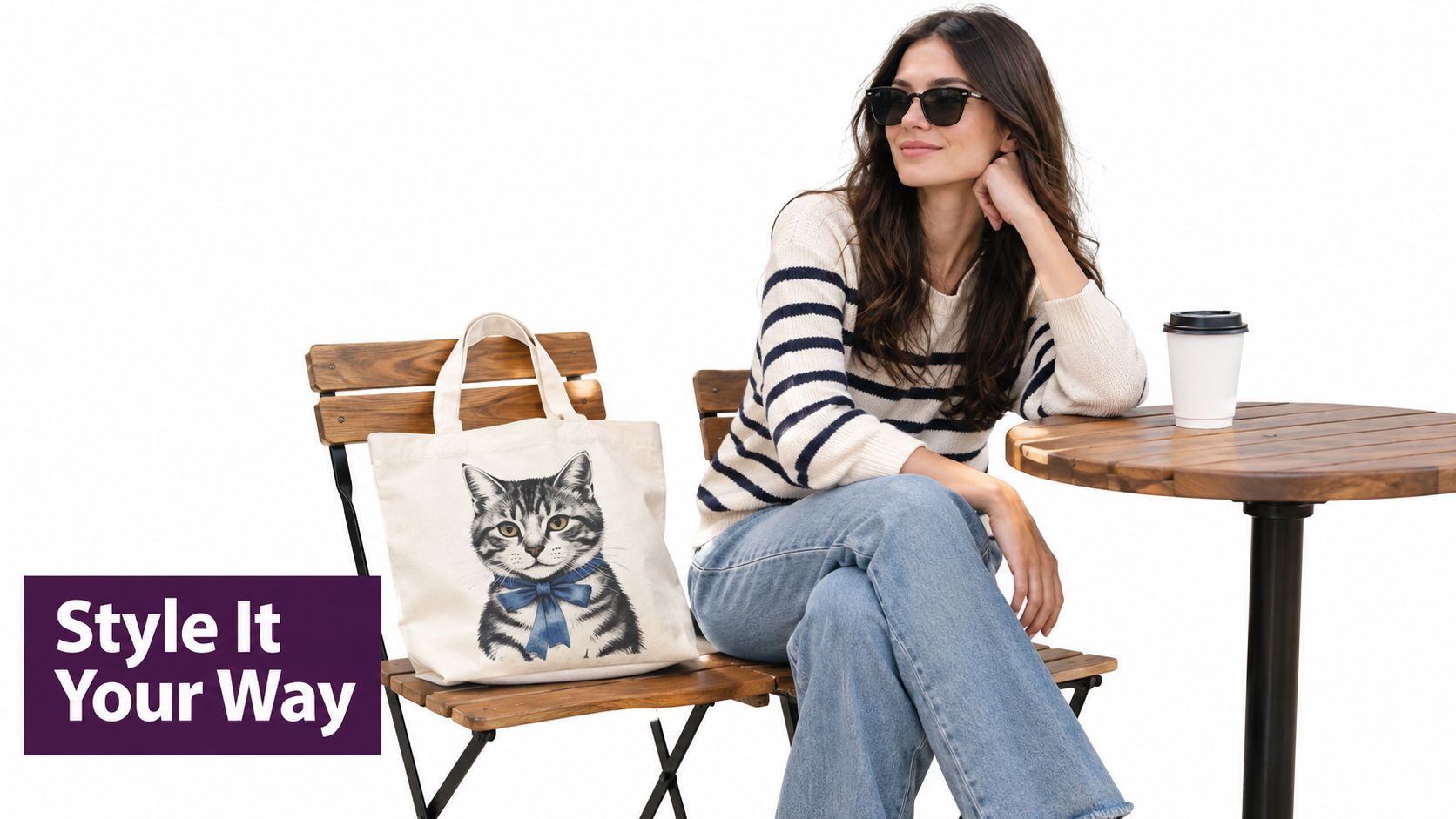 A woman wearing a striped sweater and sunglasses sits at a small wooden table with a cat tote bag.