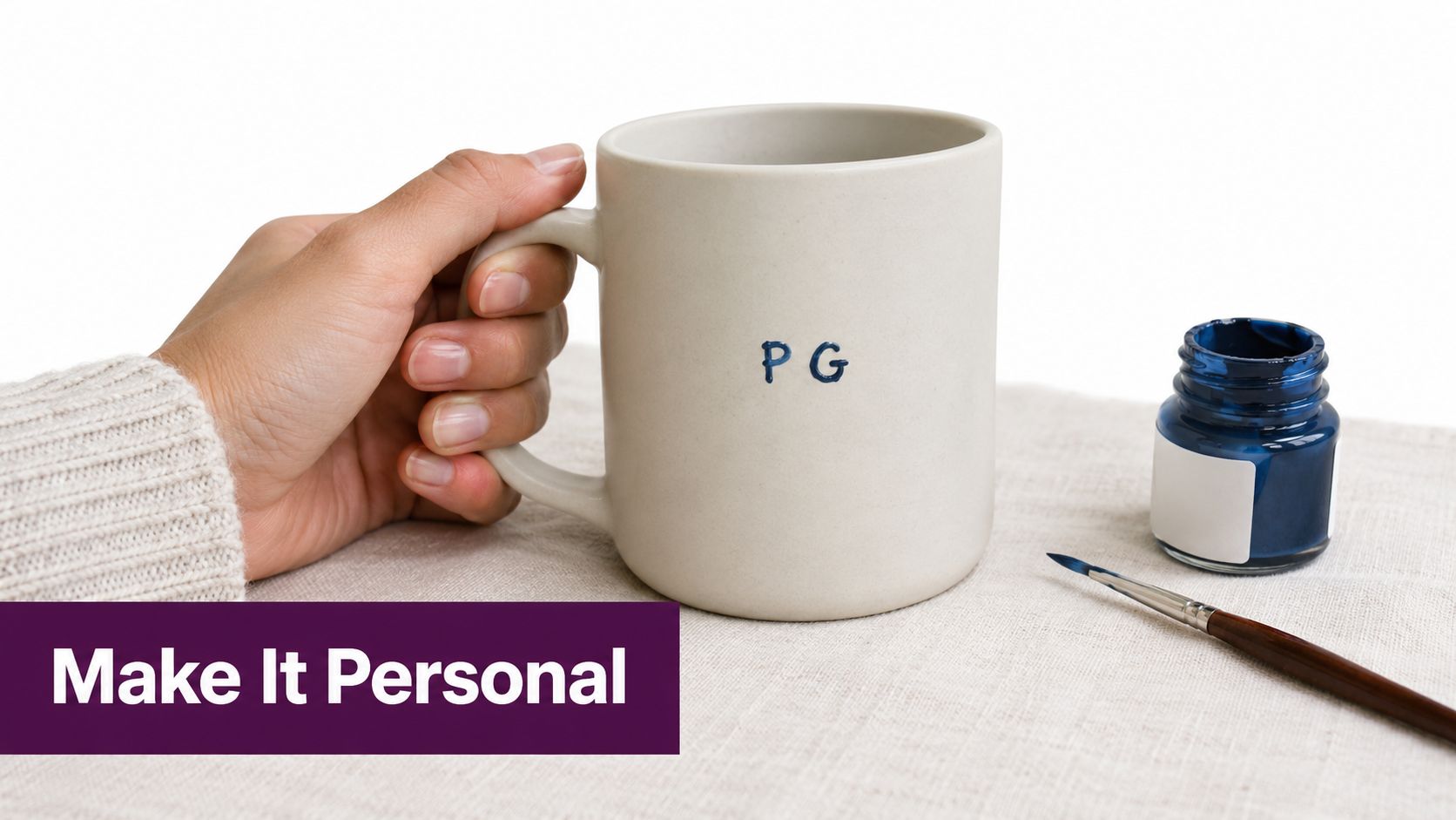 A hand holding a personalized ceramic coffee mug with the initials PG painted on the side.