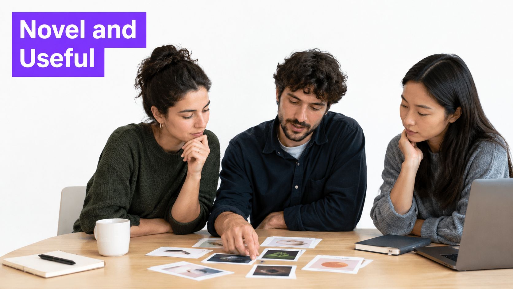 A diverse team of three professionals collaborating while reviewing creative images on a wooden meeting table.