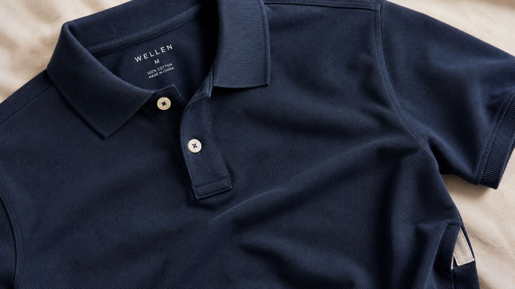 A close-up view of a dark blue Wellen brand polo shirt on a textured background.