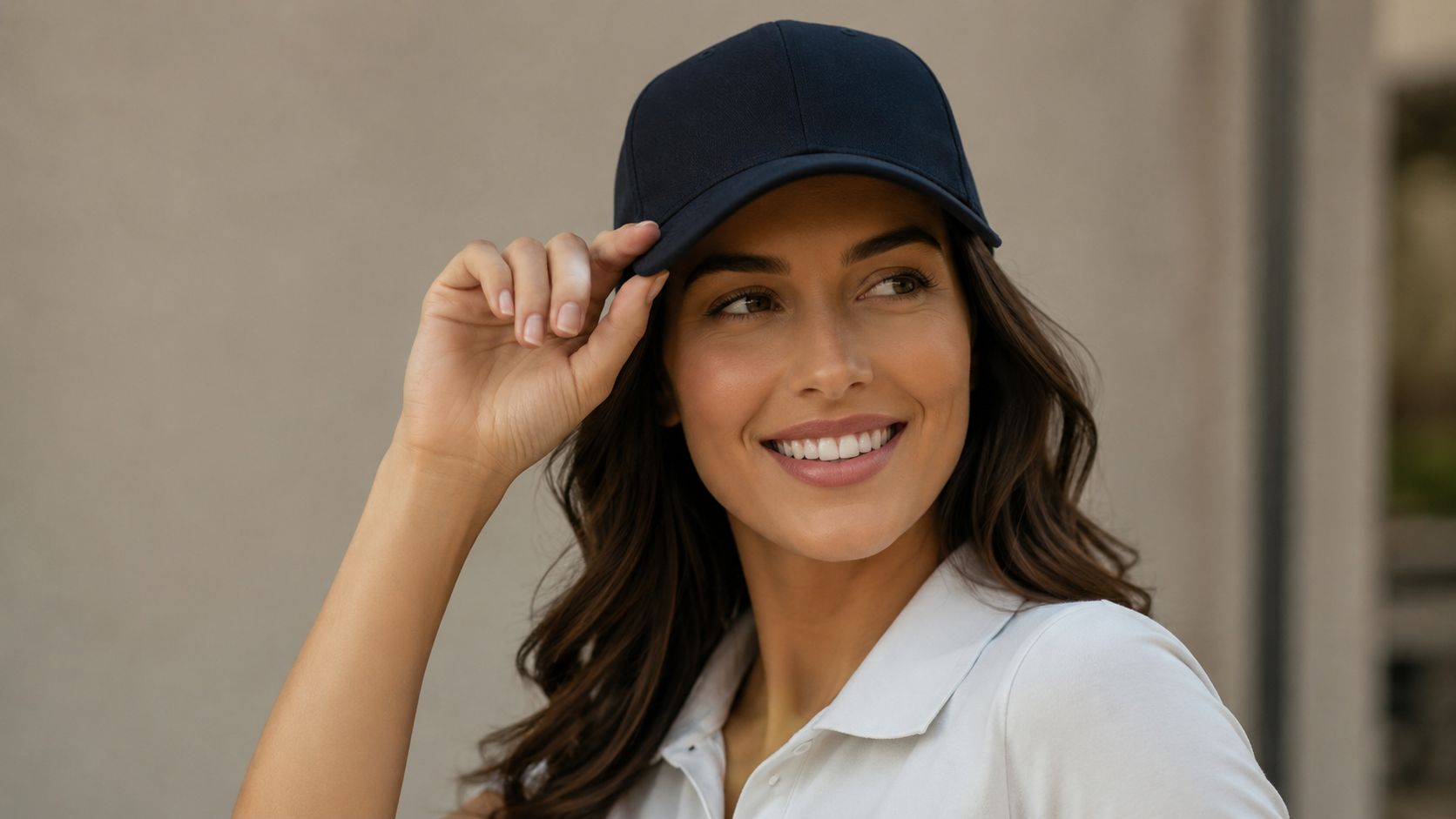 A smiling woman wearing a dark navy baseball cap and a white polo shirt looking away