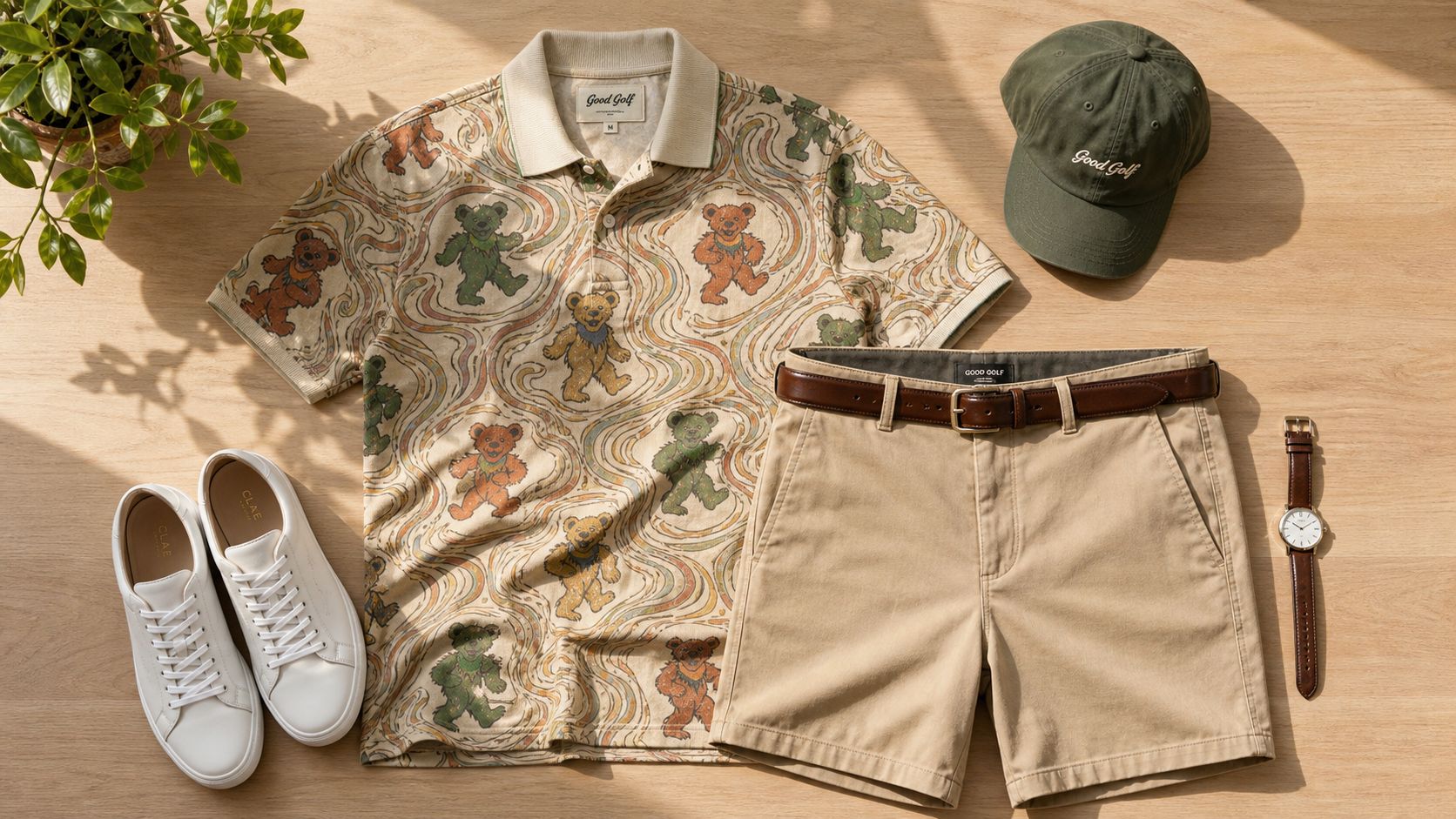A flat lay of a Grateful Dead golf shirt, khaki shorts, white sneakers, olive hat, and wristwatch.