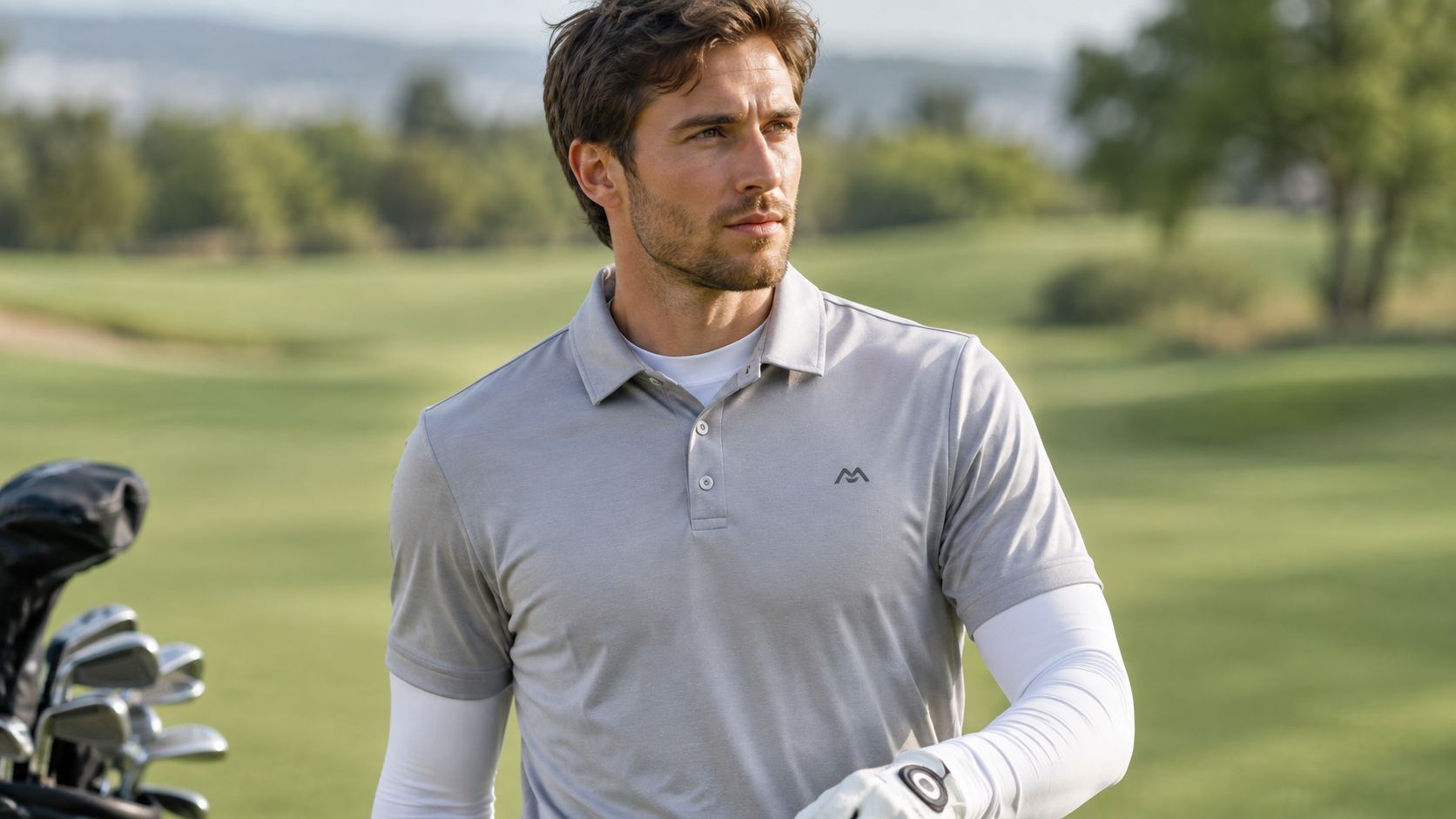 A handsome golfer wearing a grey polo shirt and white base layers standing on a green course.