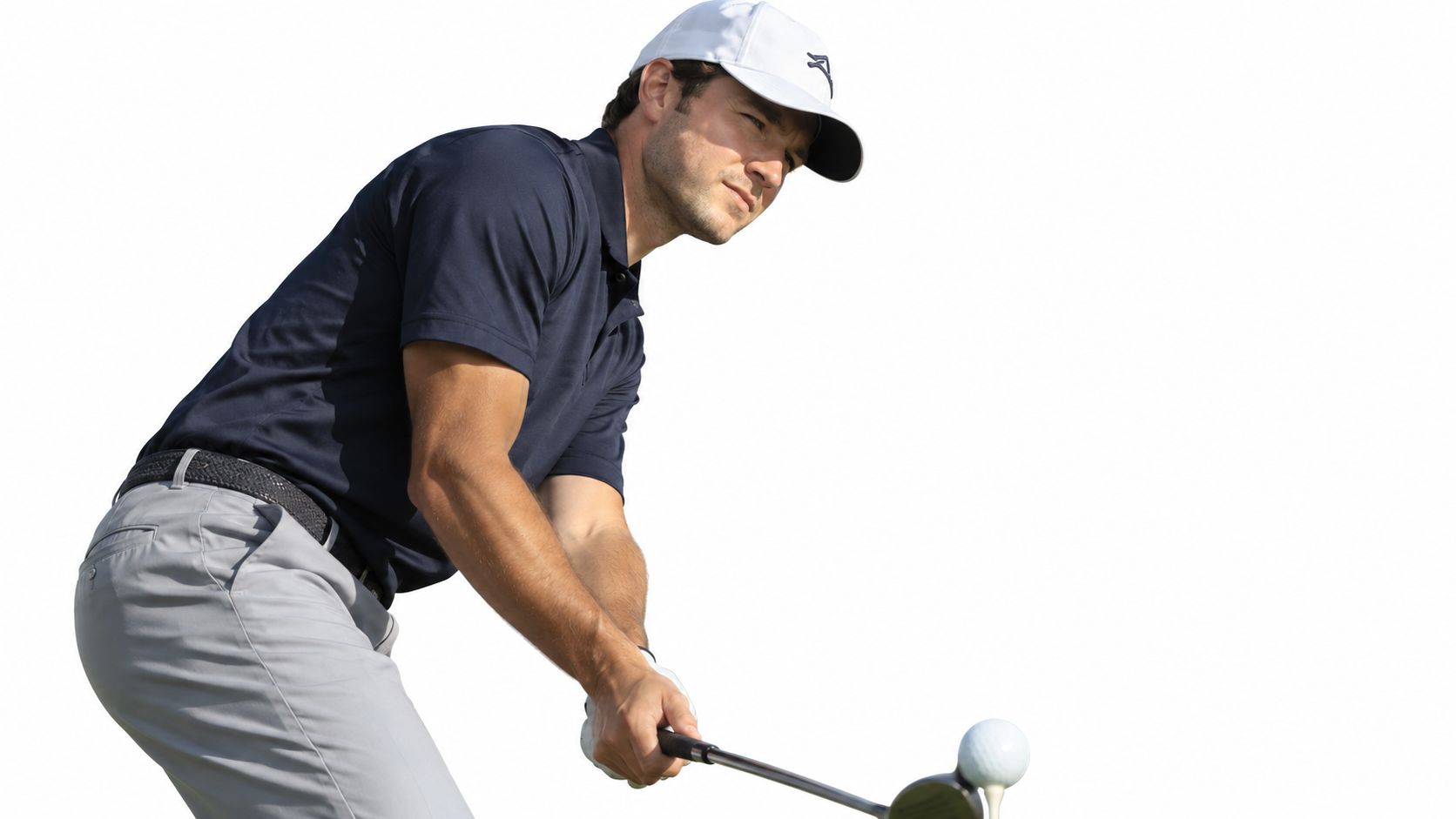 A professional male golfer wearing a white cap about to strike a golf ball with his club.