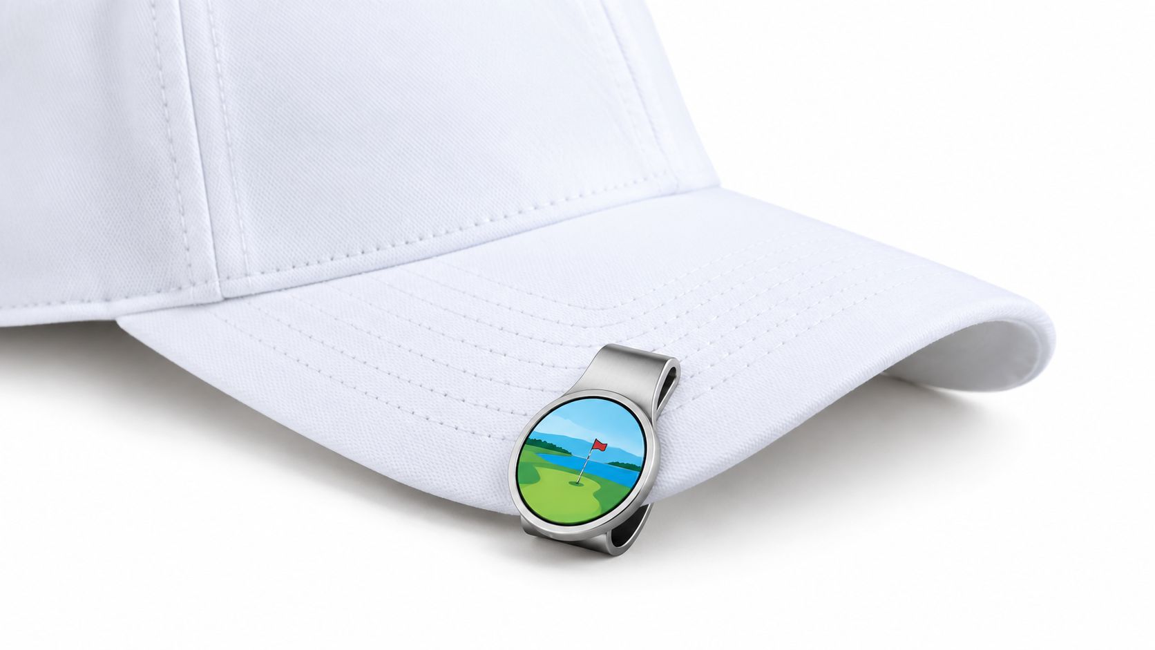 A silver magnetic golf cap clip featuring a scenic golf course illustration attached to a white cap.