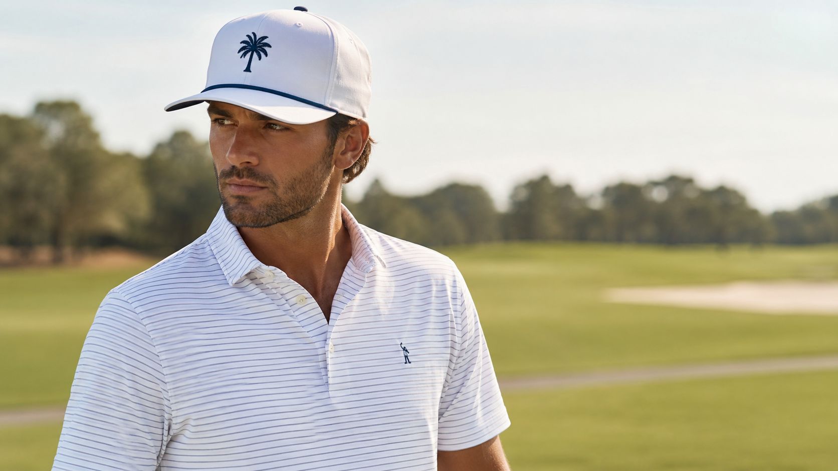 A man wearing a white polo shirt and a white baseball cap with a palm tree logo.
