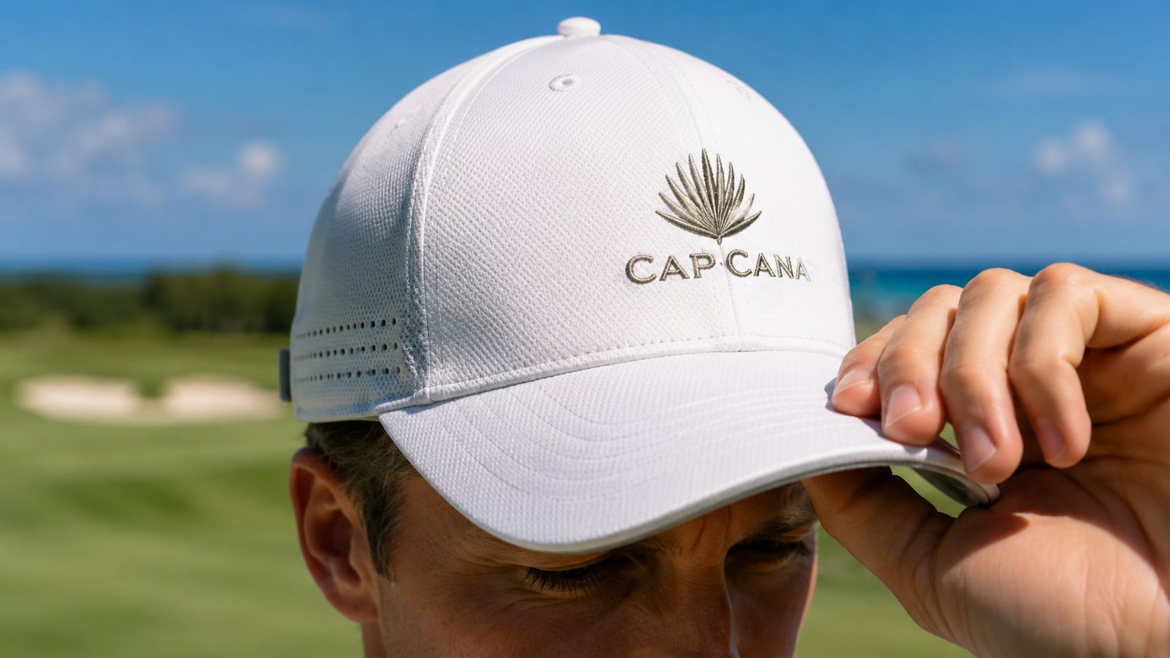 A close-up shot of a man wearing a white Cap Cana branded golf hat outdoors.