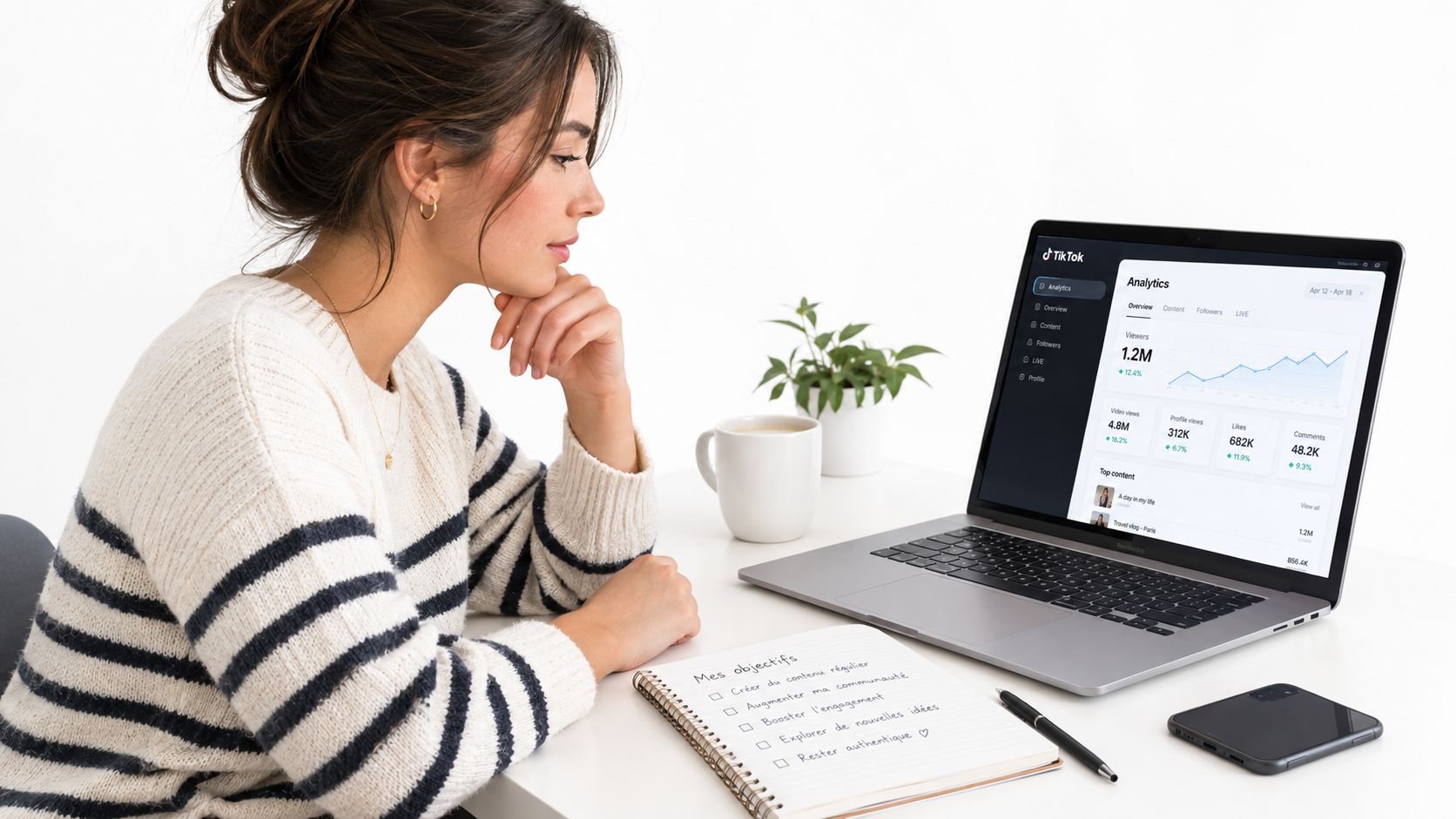 Une jeune femme consulte les statistiques de son compte TikTok sur un ordinateur portable devant un carnet.