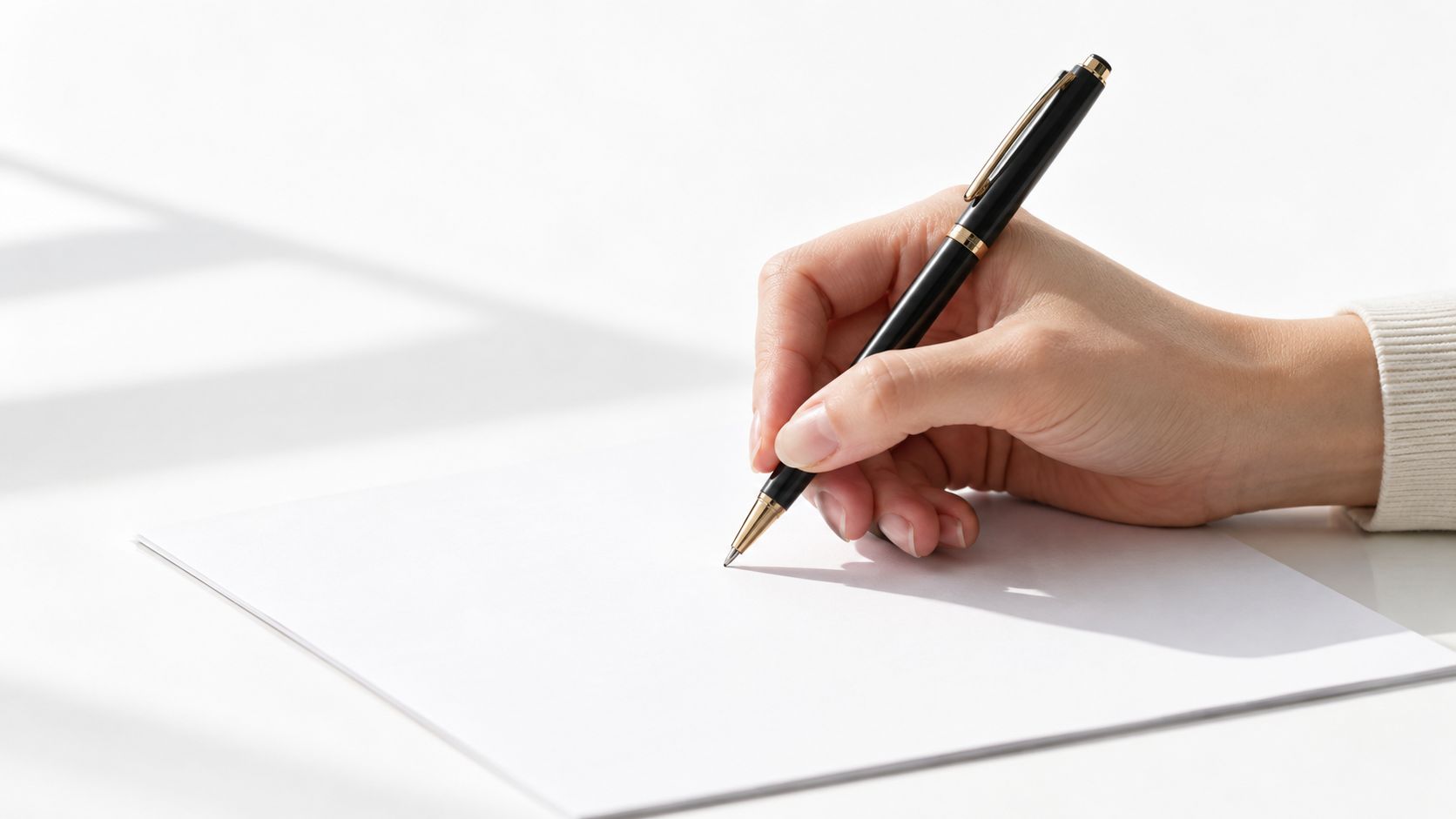 A close-up view of a hand holding a black pen and writing on a white paper.