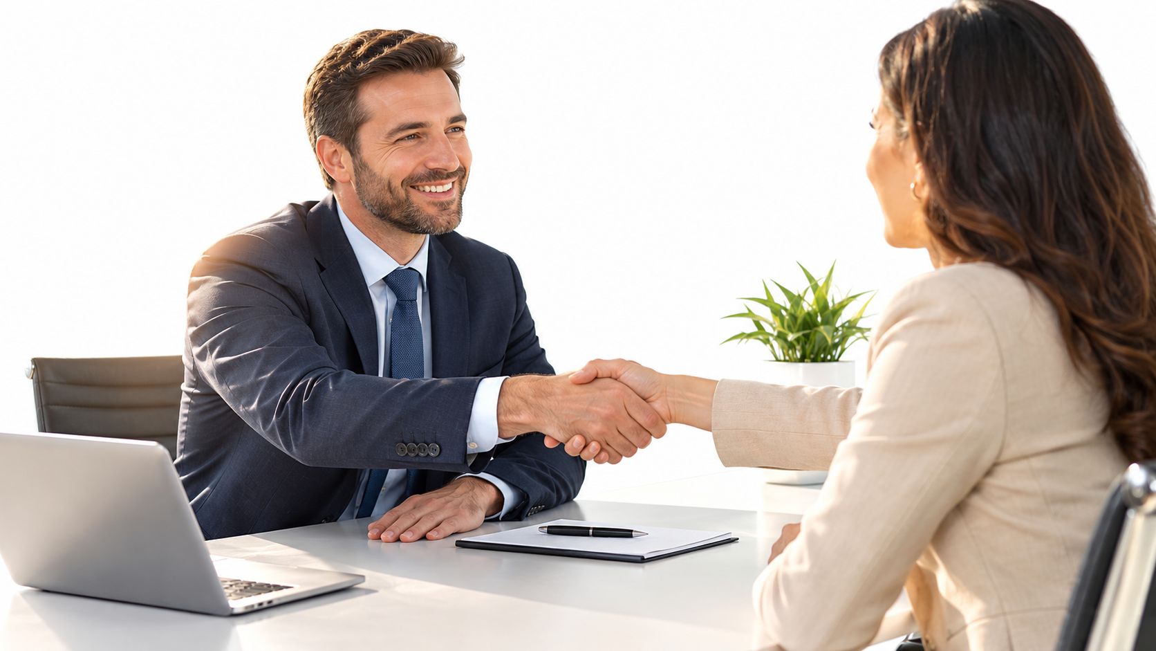 A professional man and woman shaking hands across a desk during a business meeting in an office.
