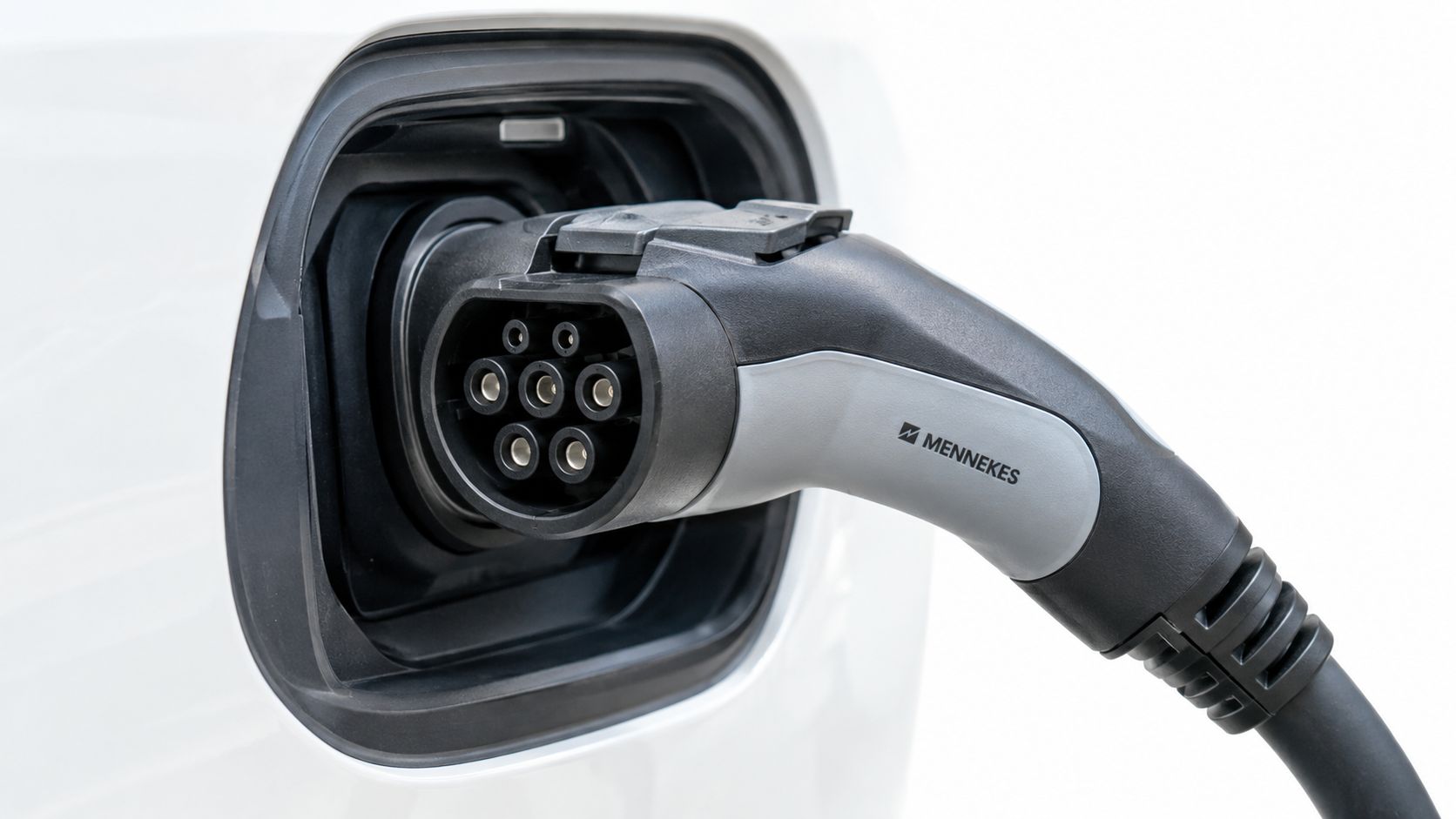 Un cargador eléctrico tipo Mennekes conectado al puerto de carga de un coche eléctrico de color blanco.
